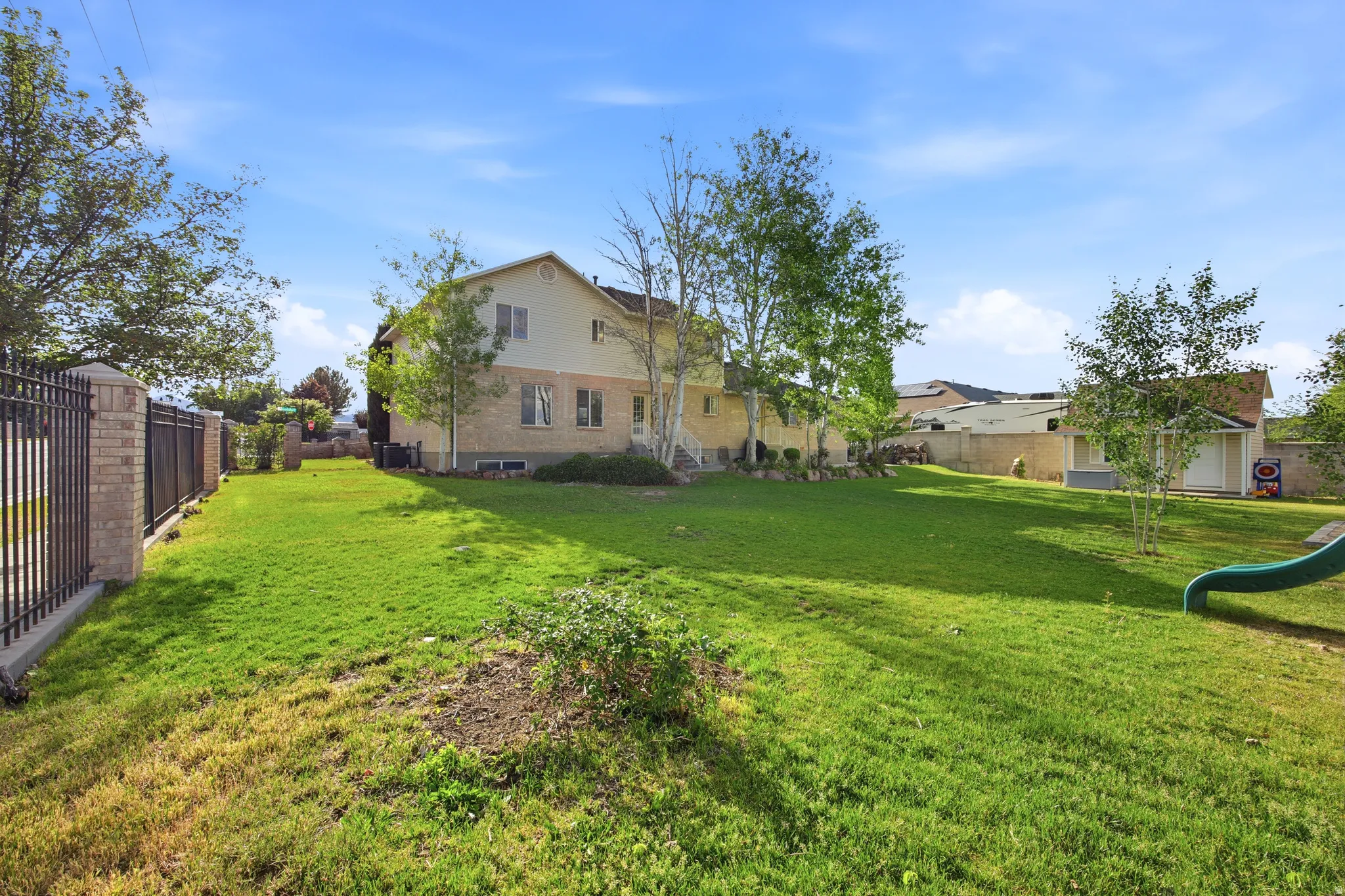 Expansive backyard featuring a manicured lawn, mature trees, and a two-story residence with a brick and siding exterior