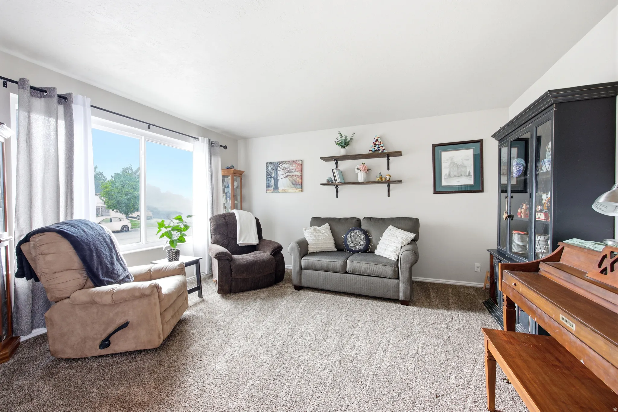 Spacious living area featuring light gray walls, plush carpeting, and a large window with white trim