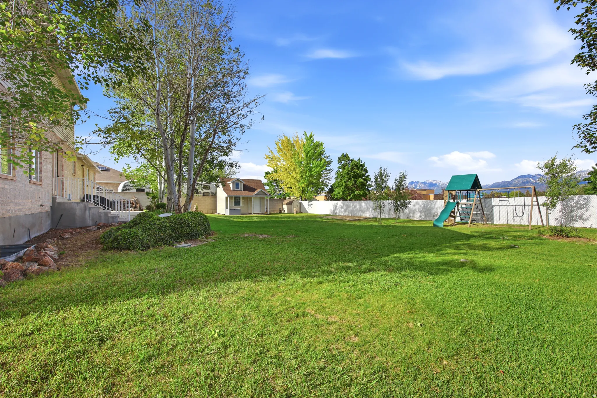 Expansive rear yard featuring a manicured lawn, established perimeter trees, and a white privacy fence