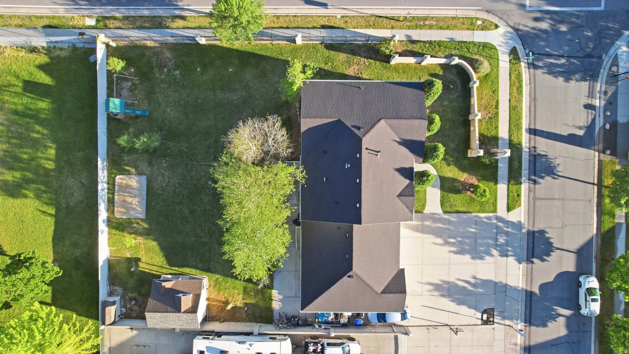 Expansive property featuring a multi-gabled main residence with dark shingle roofing, a detached shed with a matching roof, a large grassy yard, and a concrete driveway