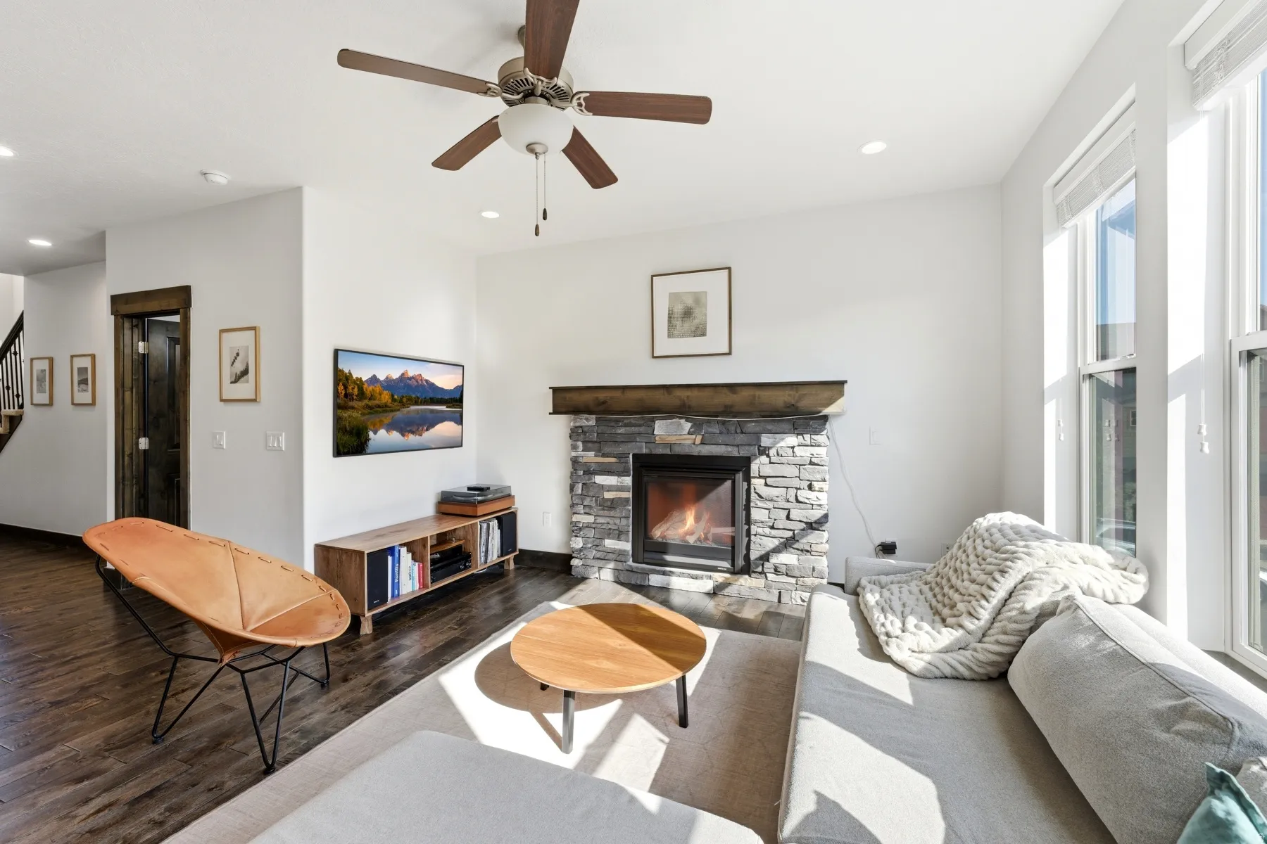 Living area featuring a stone fireplace with a wood mantle, wood-finish flooring, a ceiling fan, recessed lighting, and multiple windows