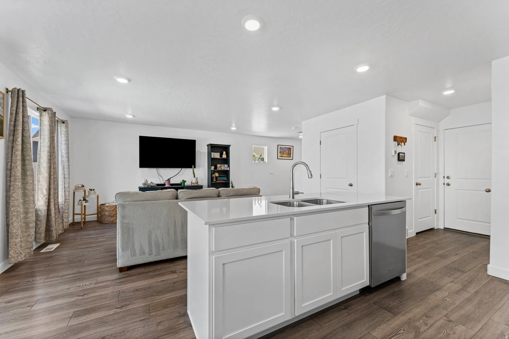 Kitchen island featuring a double-basin stainless steel sink, gooseneck faucet, white shaker cabinetry, and a dishwasher