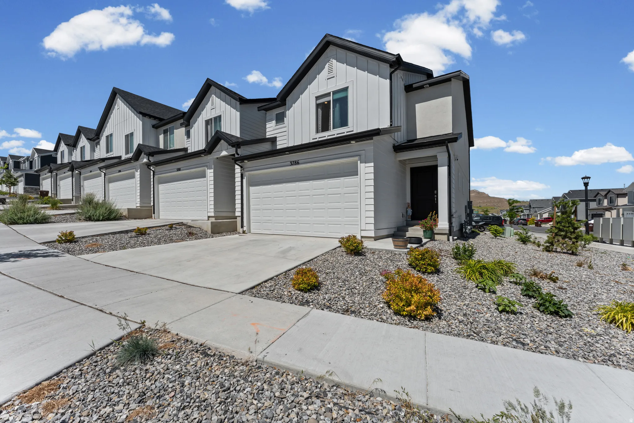 Contemporary townhome architecture featuring board and batten siding, dark trim, and a prominent front-facing garage
