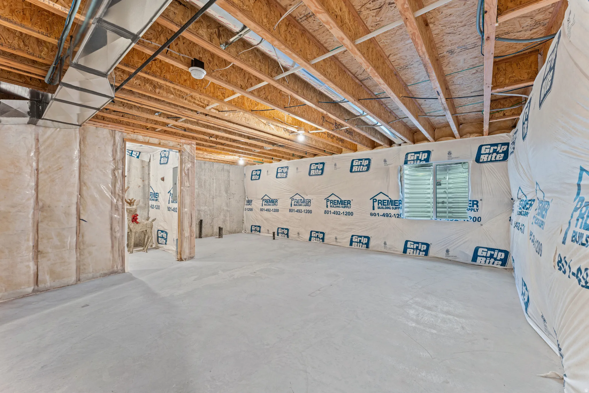 Unfinished basement featuring exposed wood joists, concrete flooring, insulated perimeter walls, and a visible egress window