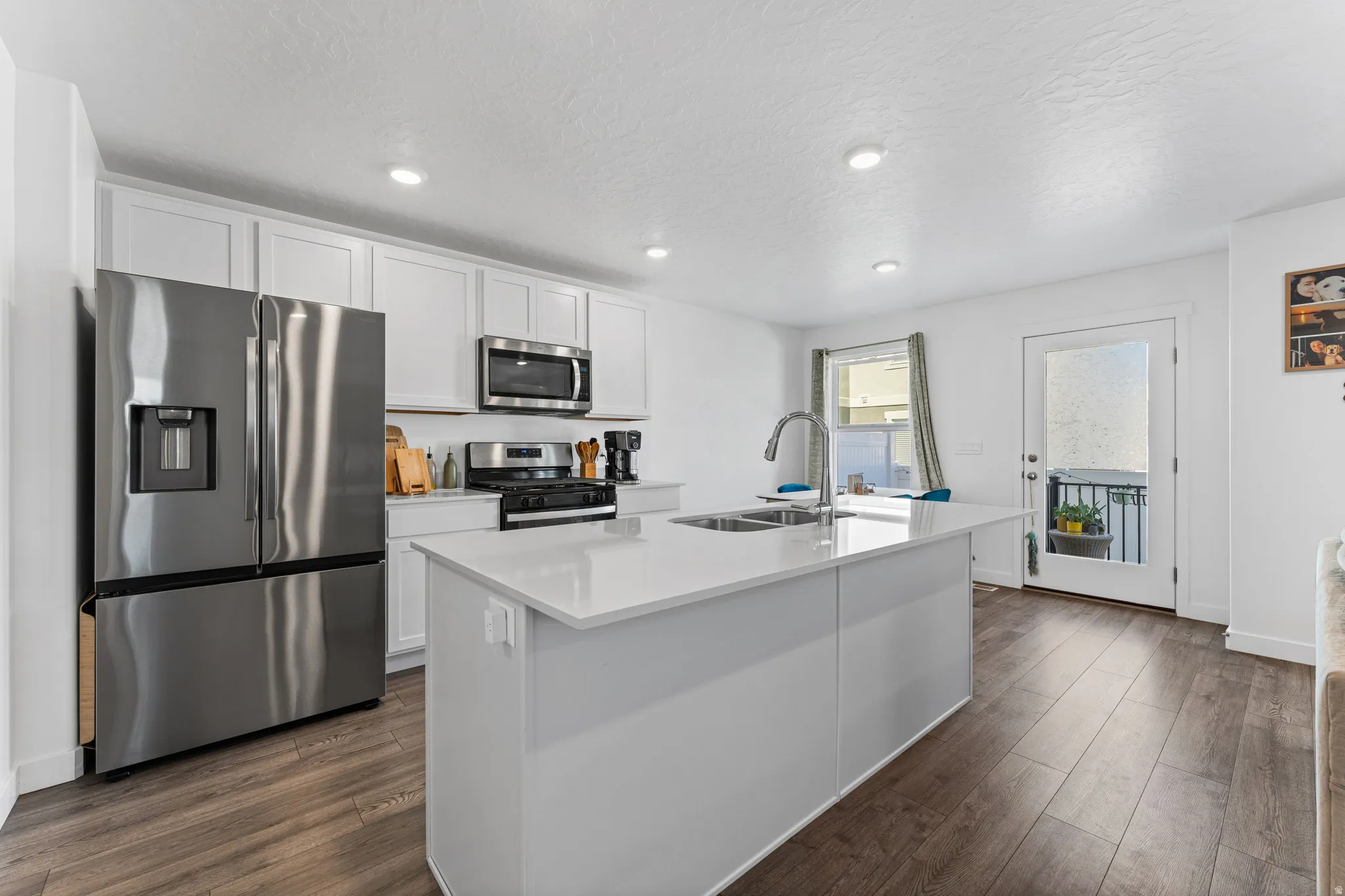 Modern kitchen featuring a central island with a double basin sink, stainless steel appliances, white cabinetry, and wood-finish flooring
