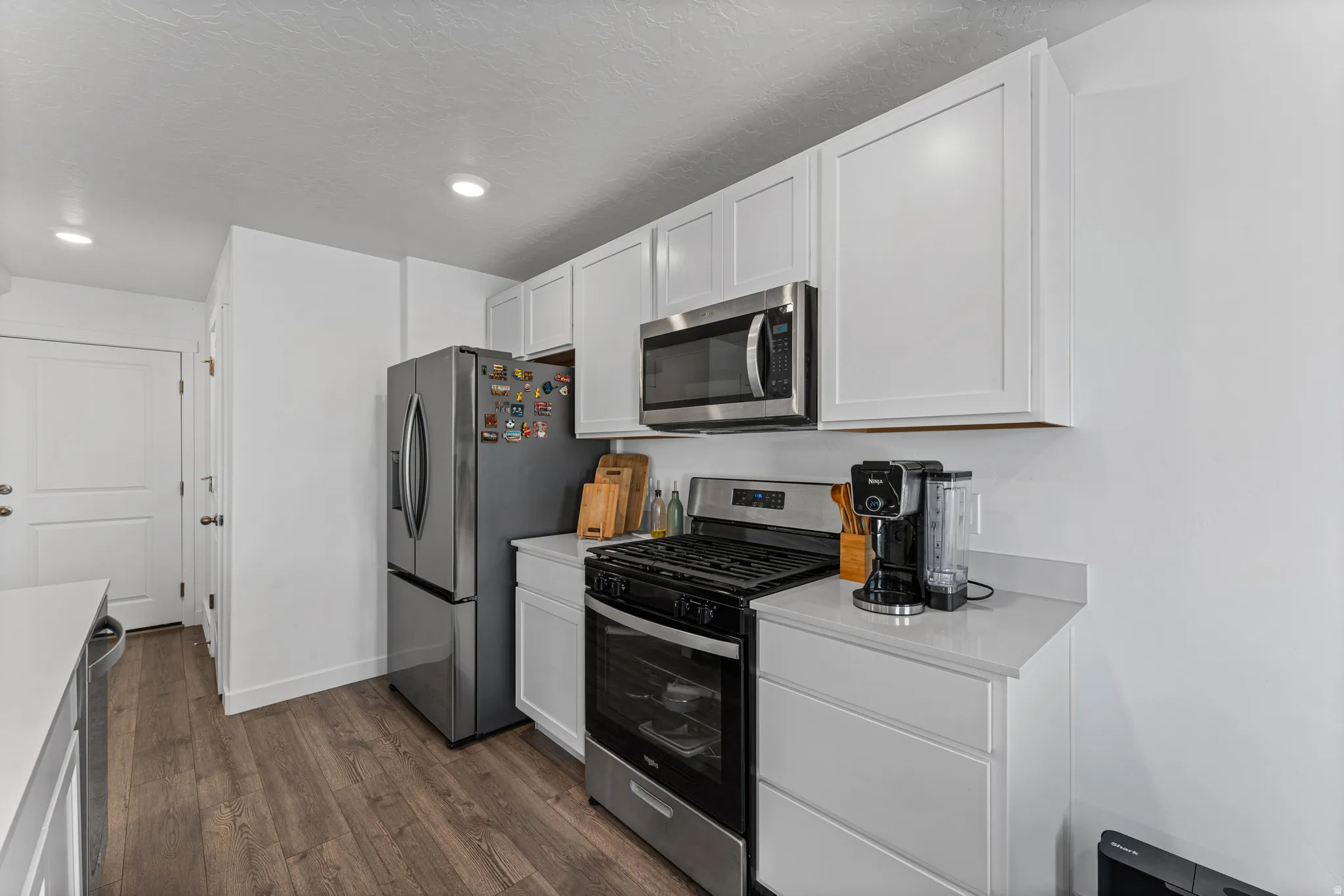 Kitchen featuring white shaker-style cabinetry, stainless steel appliances, wood-finish flooring, recessed lighting, and light-toned countertops