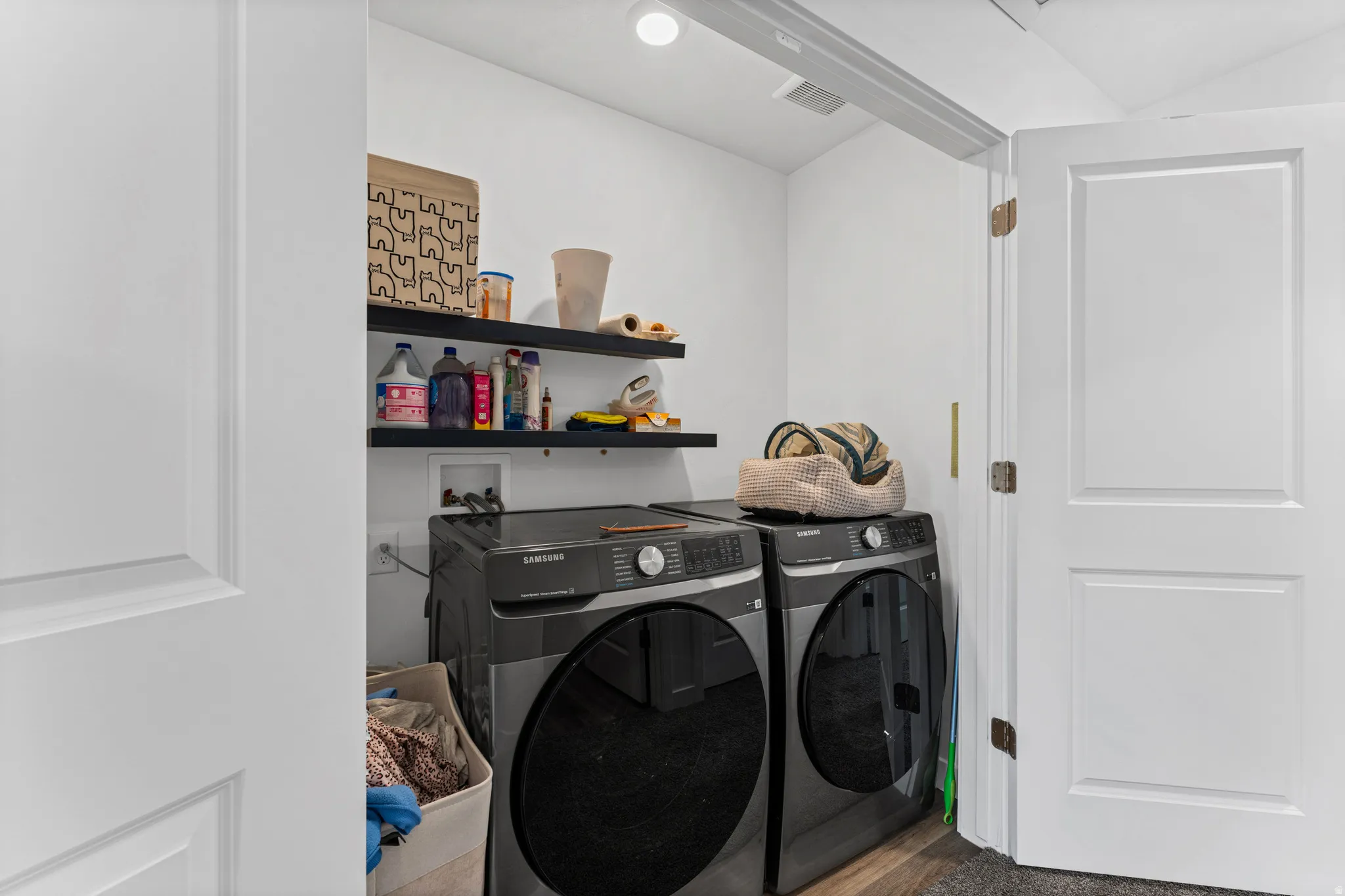Dedicated laundry area featuring a washer and dryer, two floating shelves, white walls, and wood-finish flooring