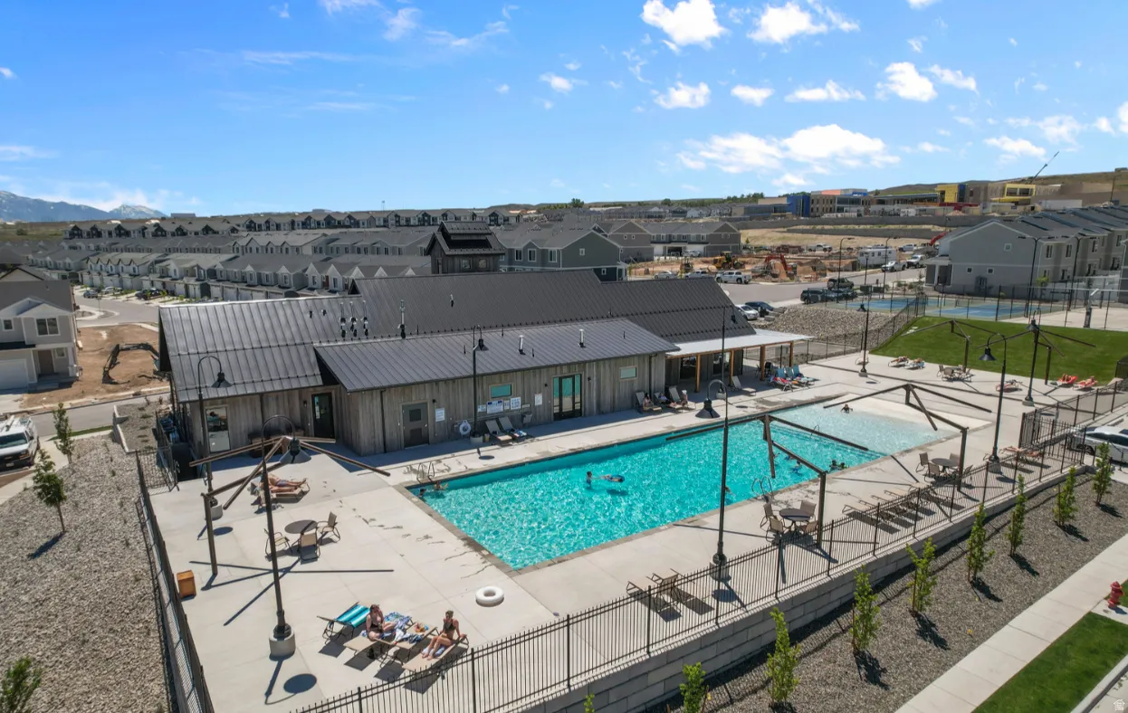 Outdoor swimming pool with integrated tanning ledge, surrounded by a concrete patio and black metal fencing
