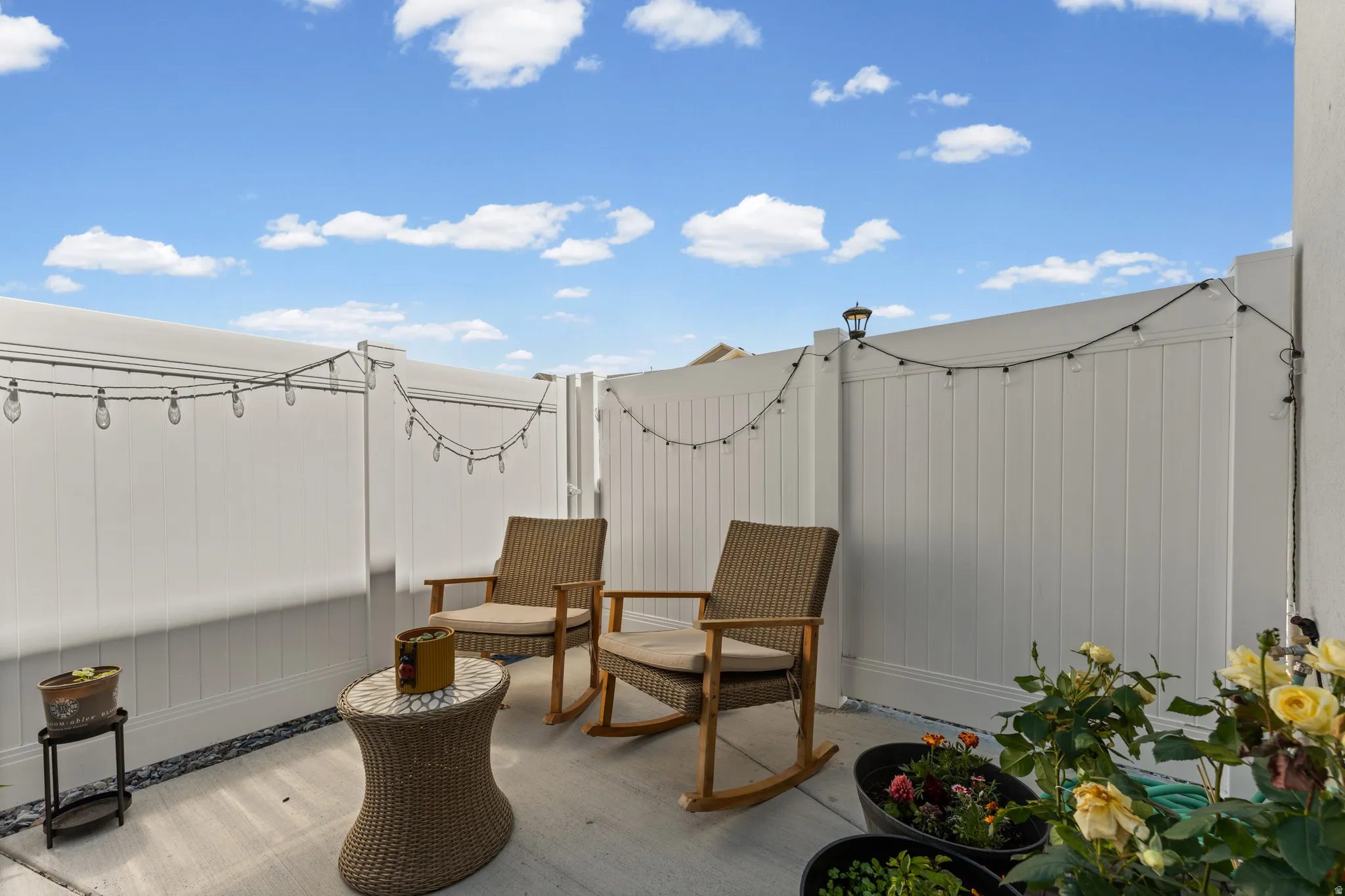 Paved patio featuring white privacy fencing, string lighting, and a gate