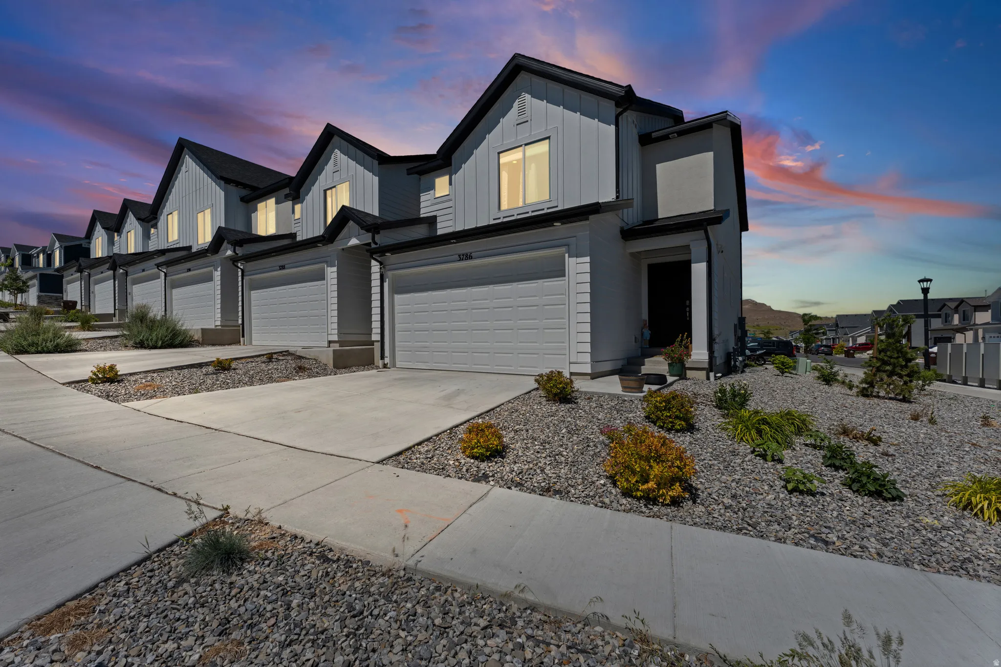 Contemporary residential exterior featuring a light gray siding facade with dark trim accents, integrated two-car garage, and concrete driveway