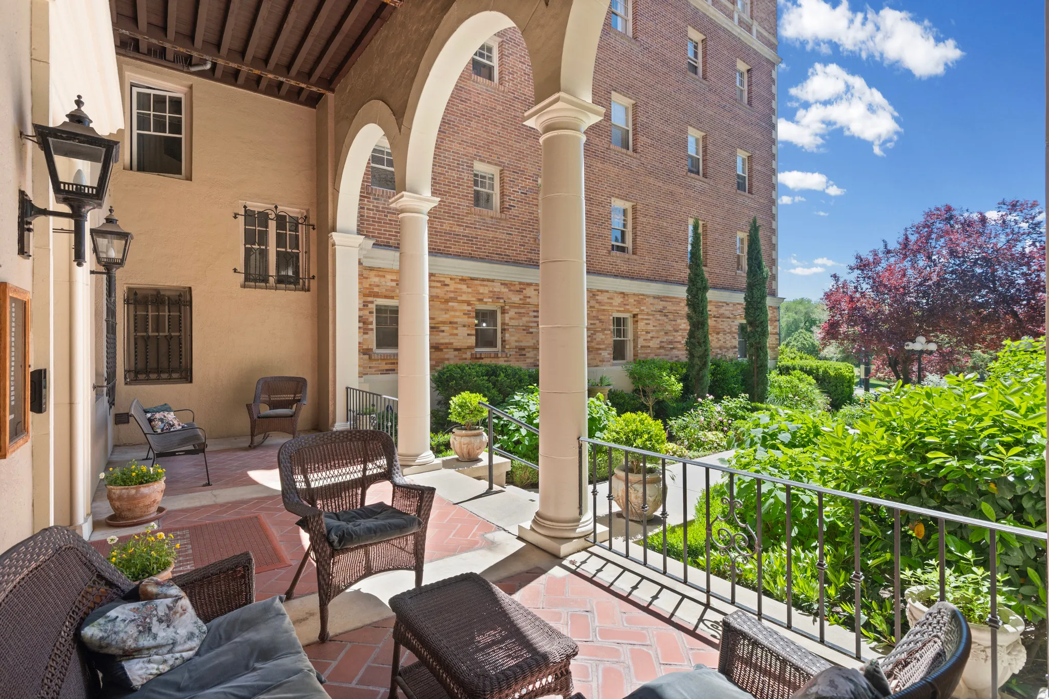 Arched loggia with terracotta tile flooring and a wrought iron railing overlooking manicured landscaping
