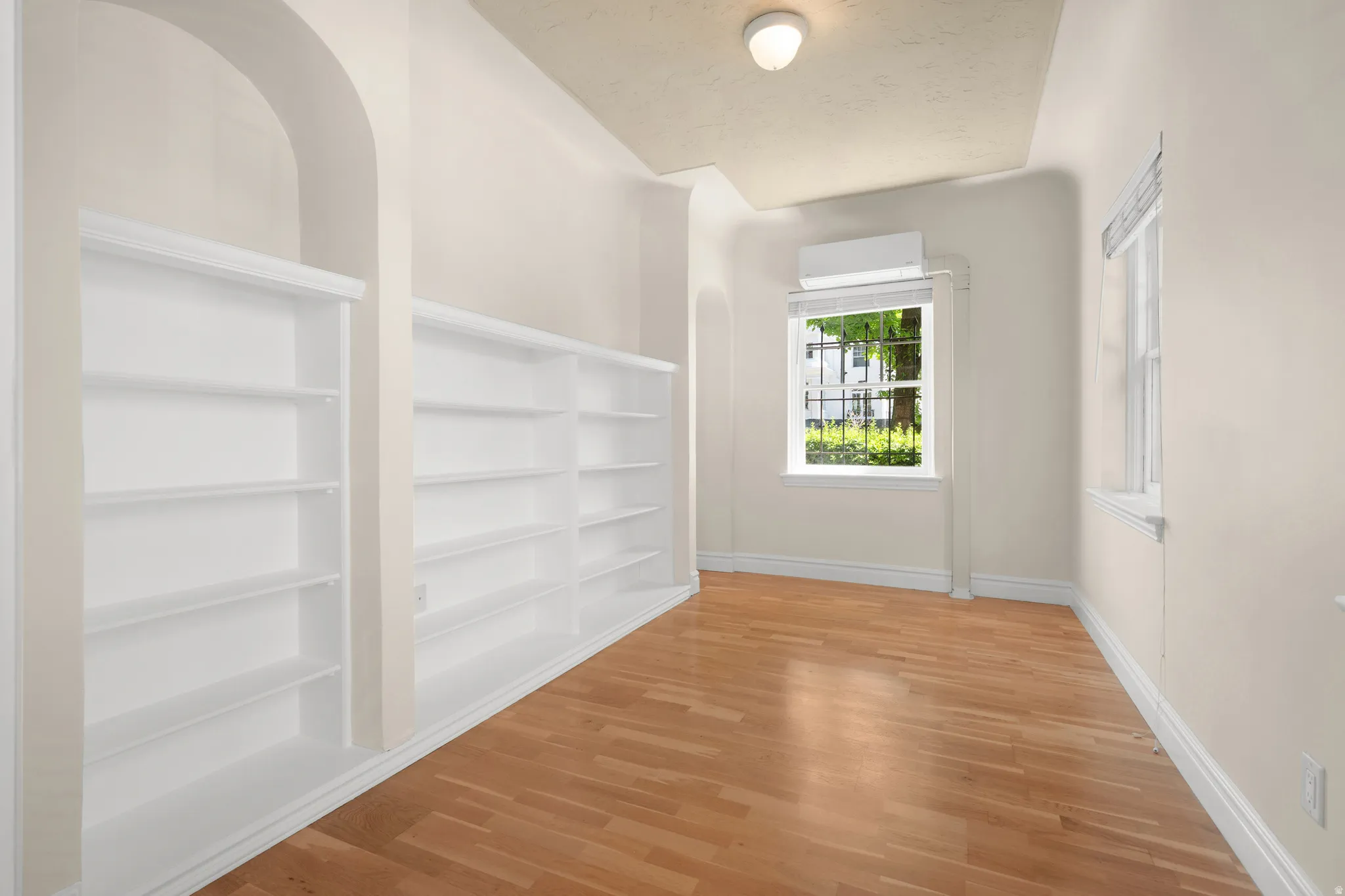 Built-in white shelving with an arched alcove, wood-finish flooring, and multiple windows providing natural light