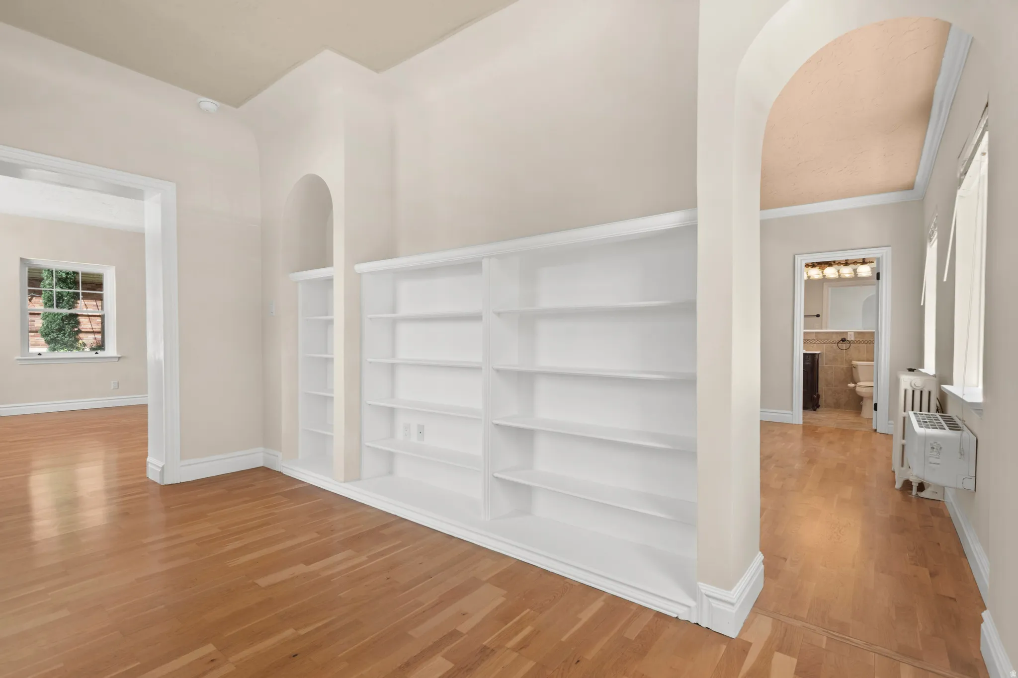 Built-in shelving with recessed alcoves, wood-finish flooring, and arched doorways