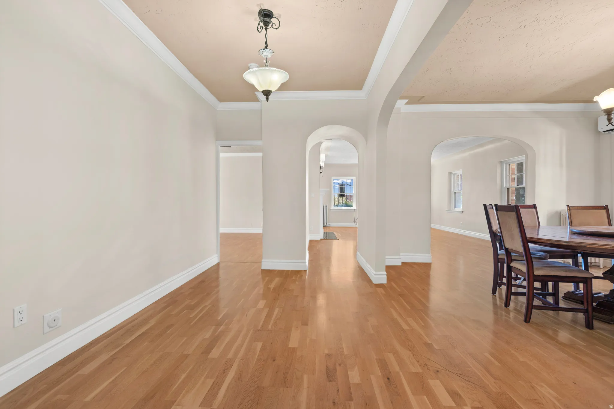 Wood-finish flooring throughout, featuring decorative ceiling fixtures, crown molding, and arched doorways