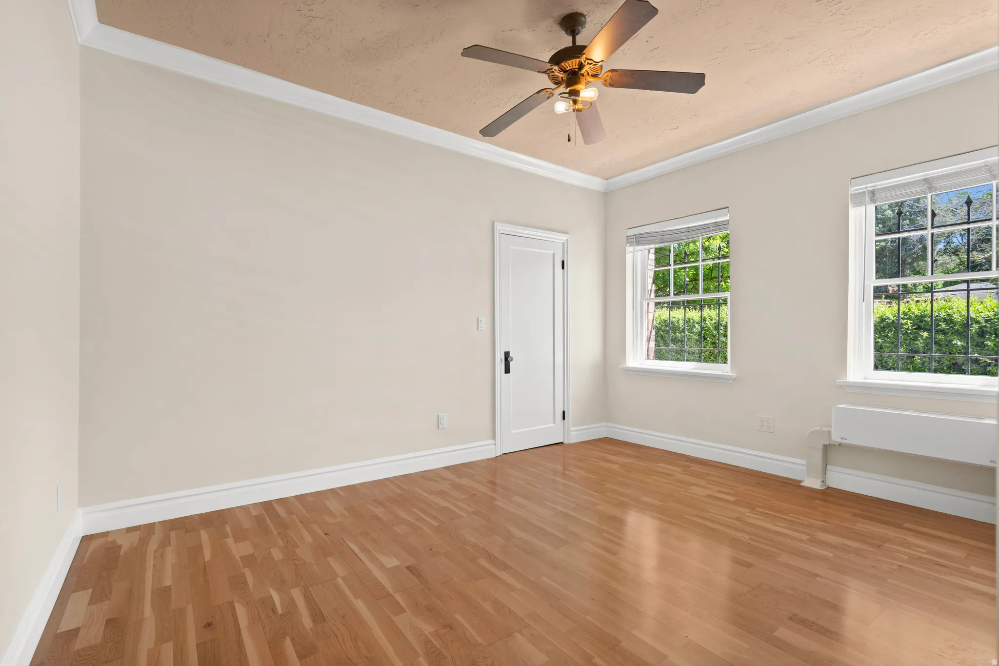 Bright interior space featuring wood-finish flooring, two large windows, a ceiling fan, and crown molding