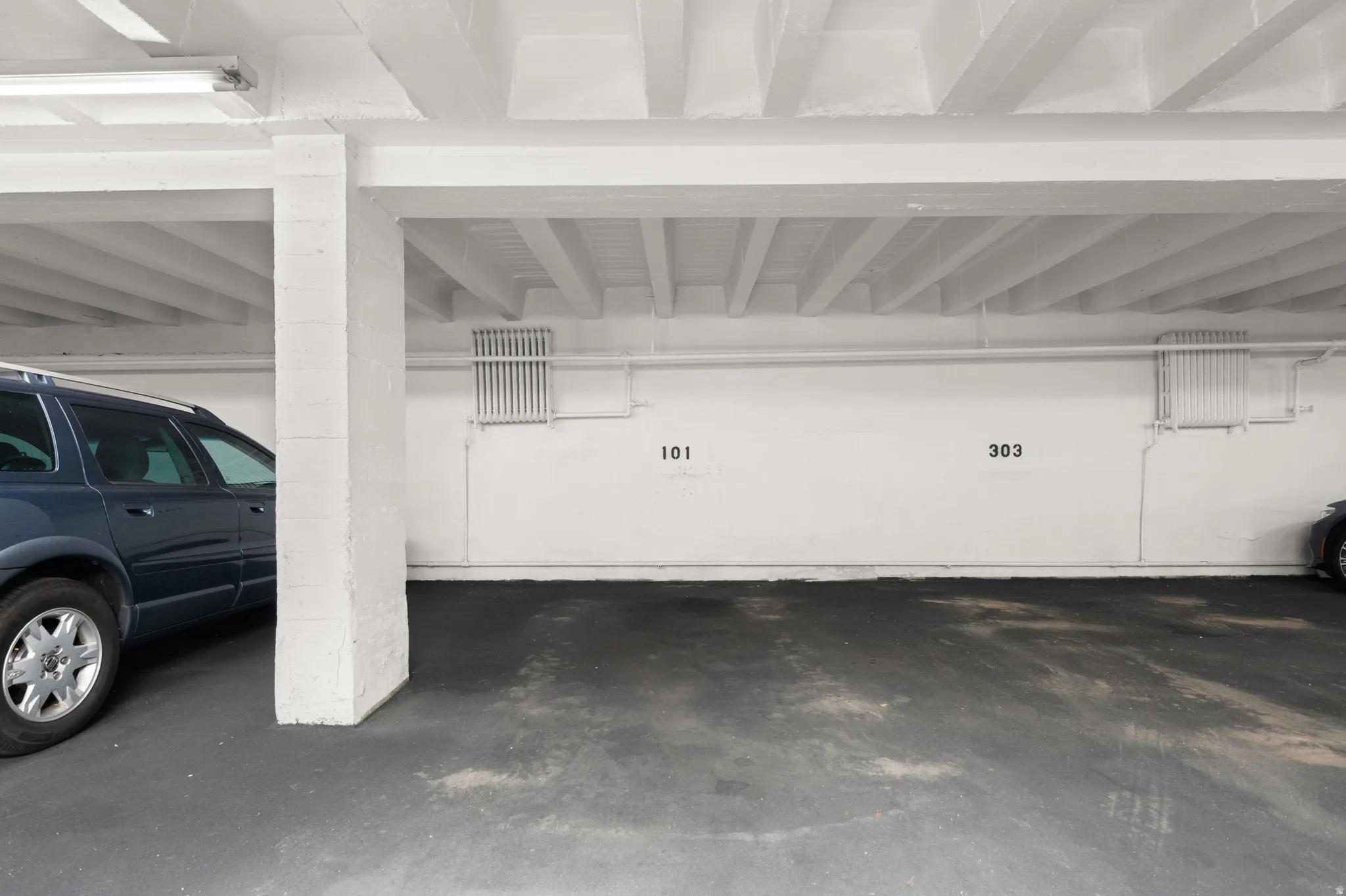 Covered parking area featuring concrete flooring, white painted walls, and overhead lighting fixtures