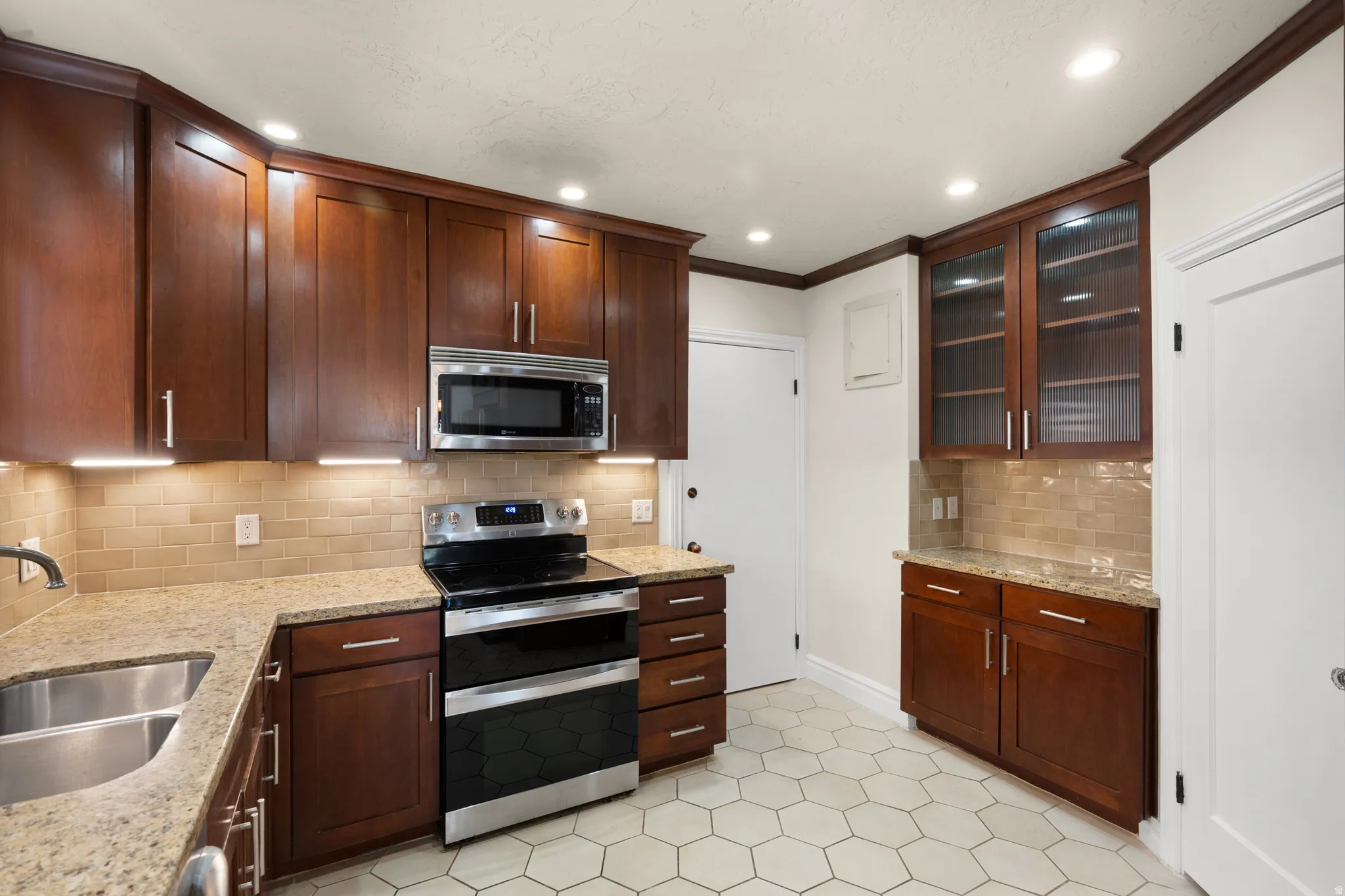 Well-appointed kitchen featuring dark wood cabinetry, stainless steel appliances, light granite countertops, and a subway tile backsplash