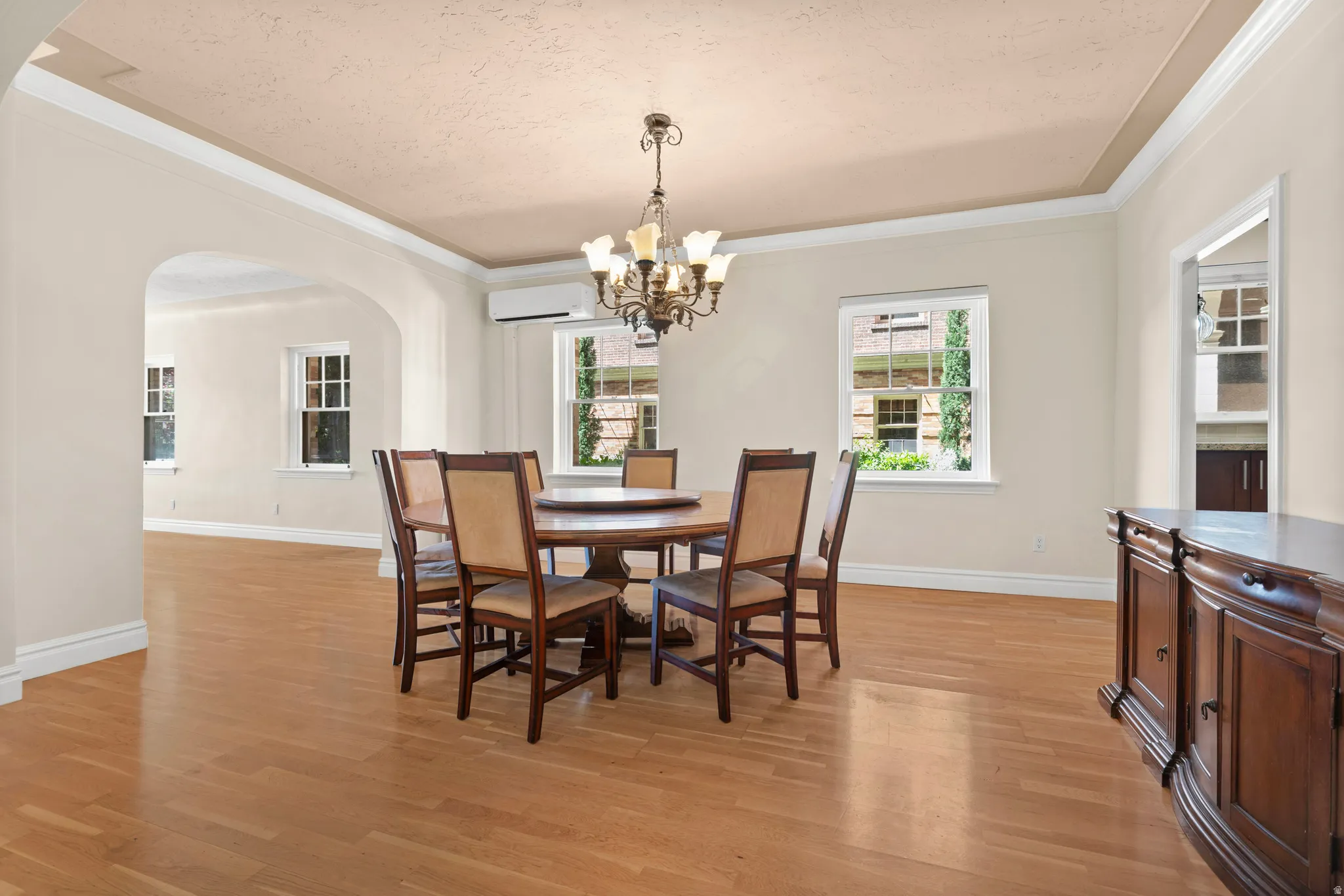 Spacious dining area featuring wood-finish flooring, a recessed ceiling with crown molding, and an arched entry