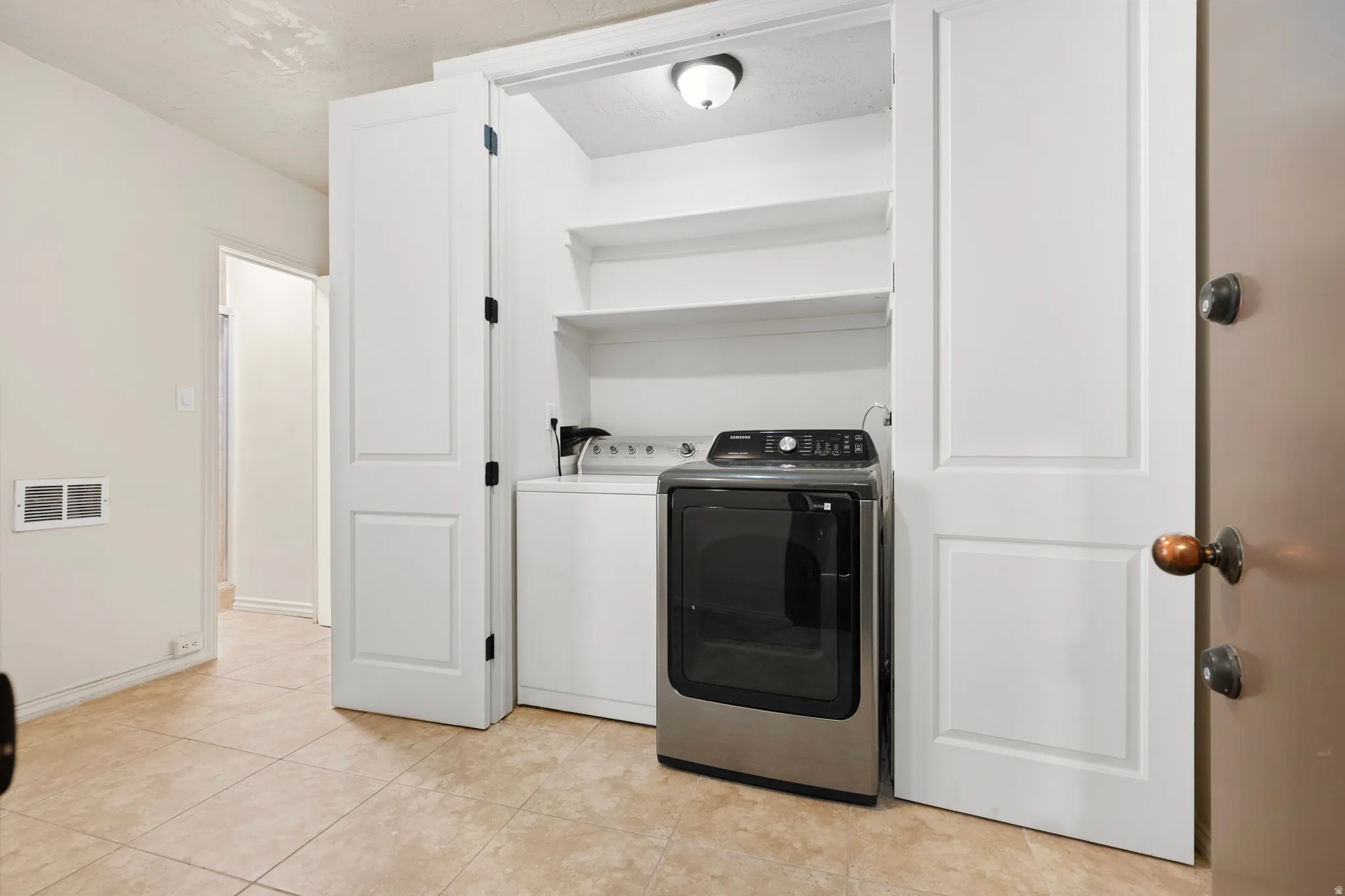 Laundry closet featuring bi-fold doors, integrated shelving, and a ceiling-mounted light fixture