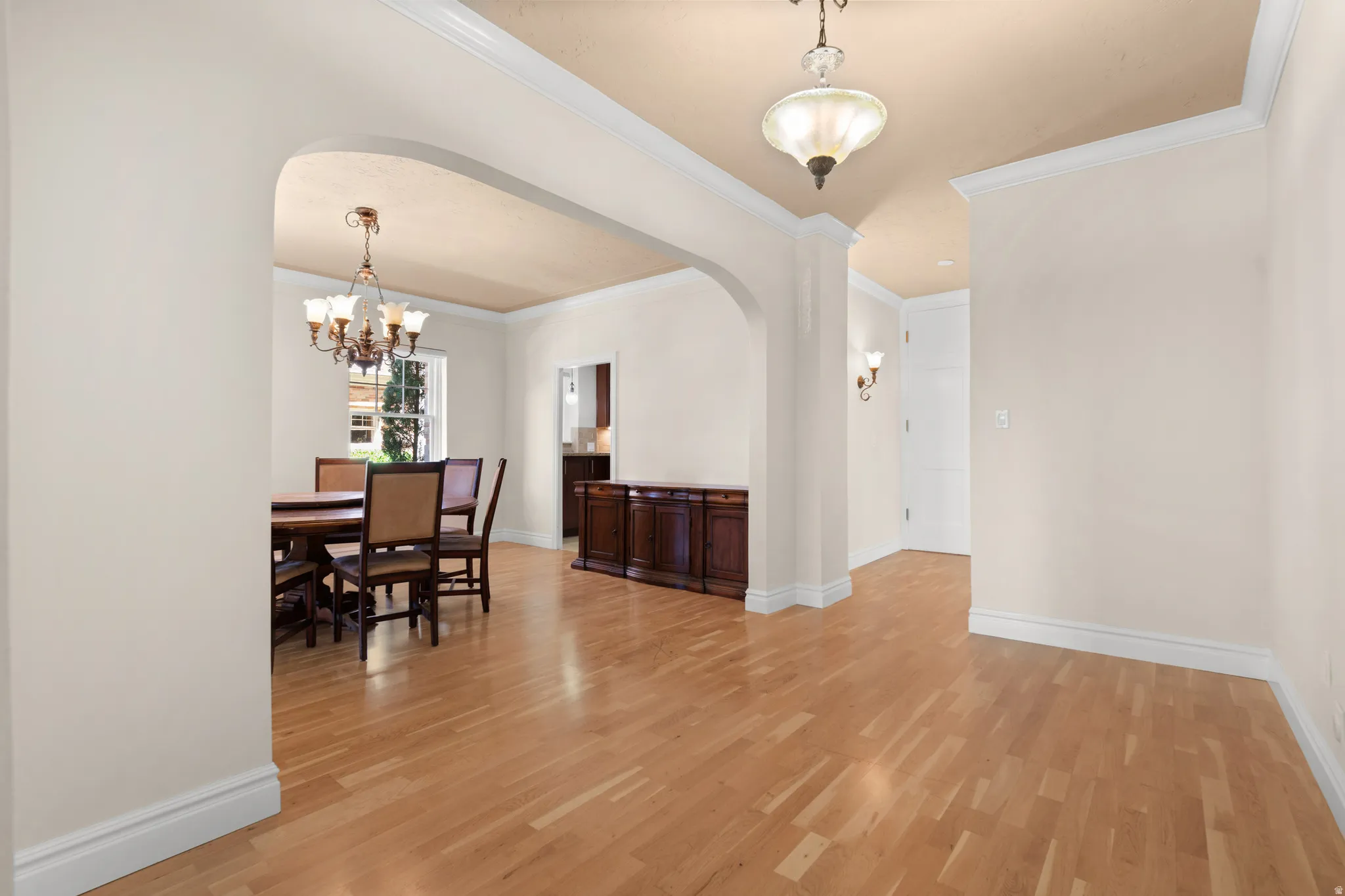 Hardwood flooring throughout, arched doorway, crown molding, wall sconces, and built-in wood cabinetry