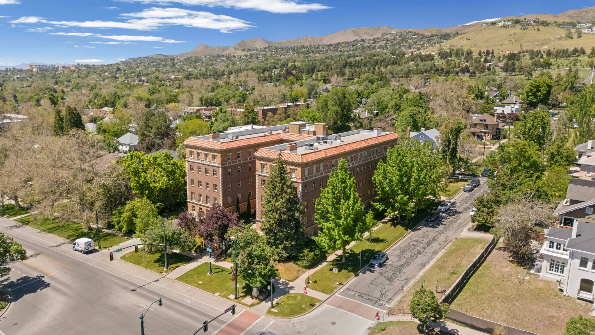 Brick multi-story building featuring terracotta-toned roof tiles, numerous windows, and established perimeter landscaping