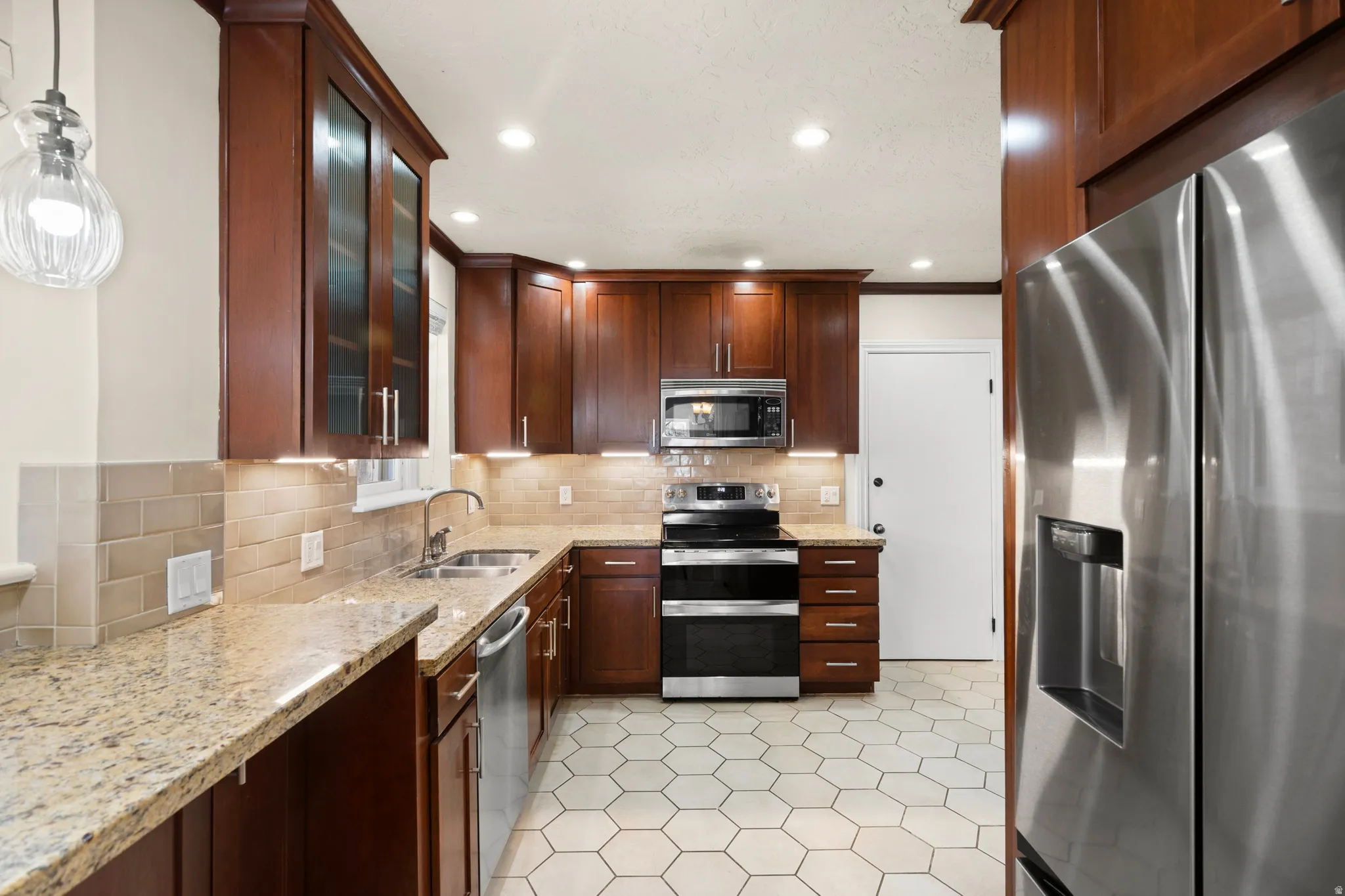 Kitchen featuring wood-finish cabinetry, light granite countertops, and a tiled backsplash