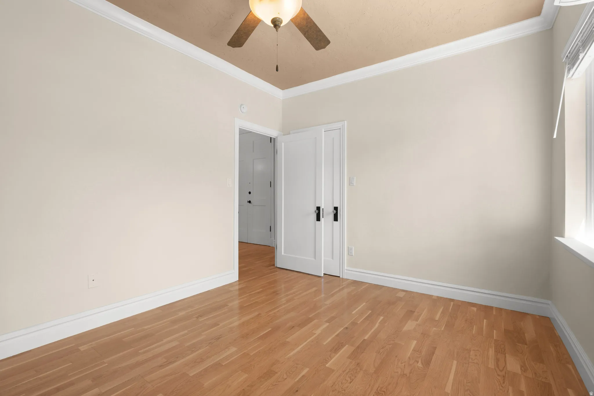Room featuring wood-finish flooring, white baseboards, and crown molding