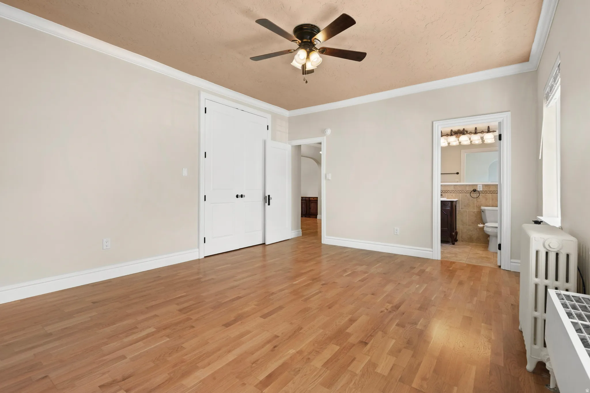 Spacious Master bedroom with wood-finish flooring, crown molding, and a ceiling fan with integrated lighting