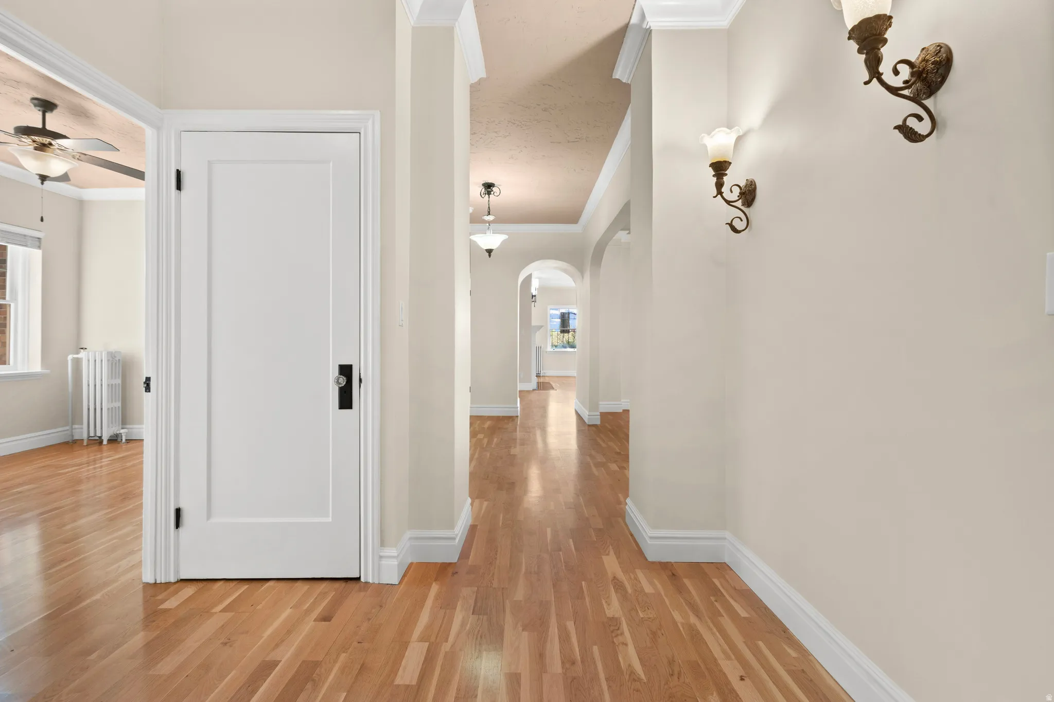 Hallway with wood-finish flooring, white trim, and decorative wall sconces