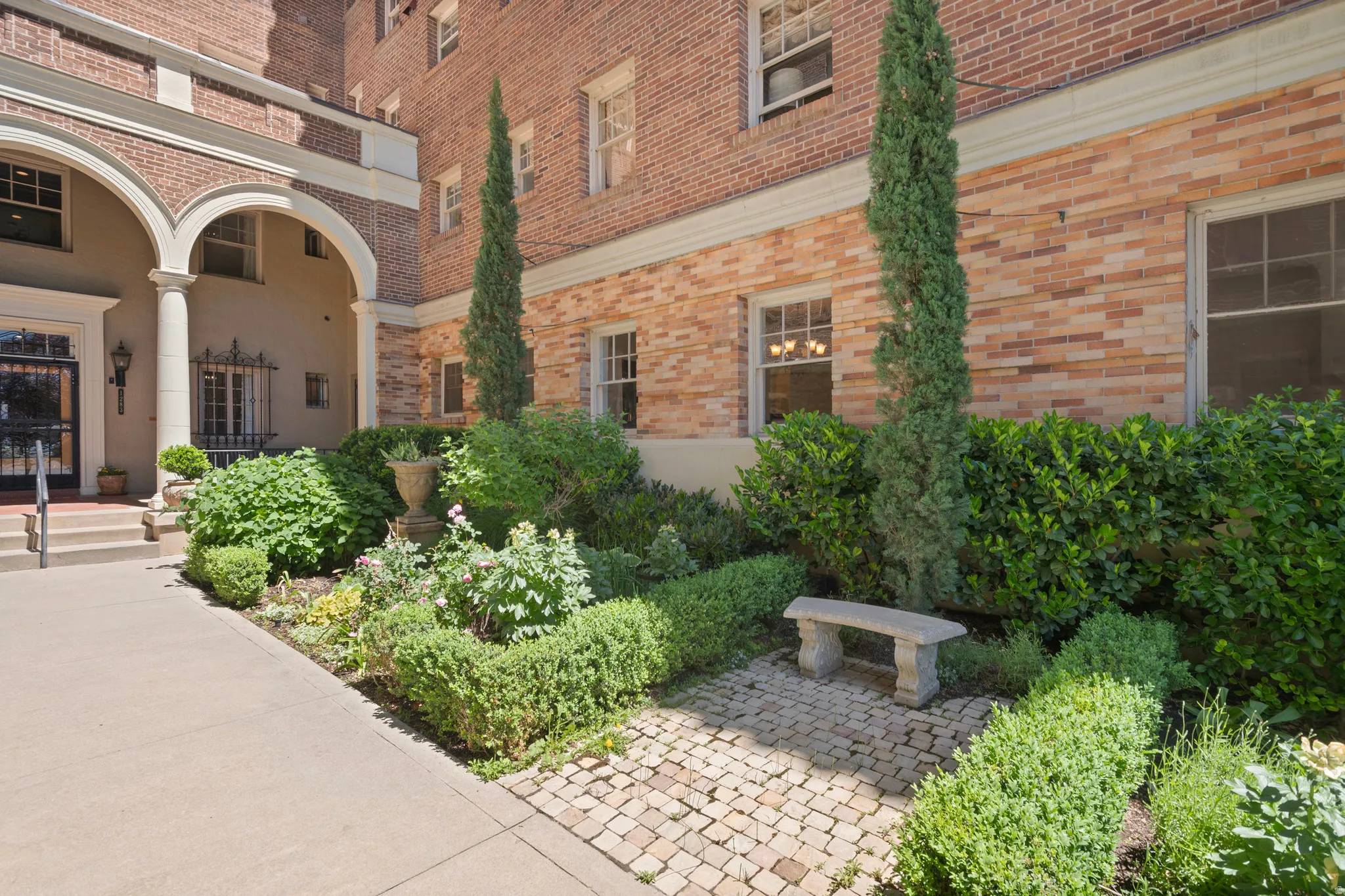 Landscaped courtyard featuring a stone bench, mature plantings, and a paver pathway