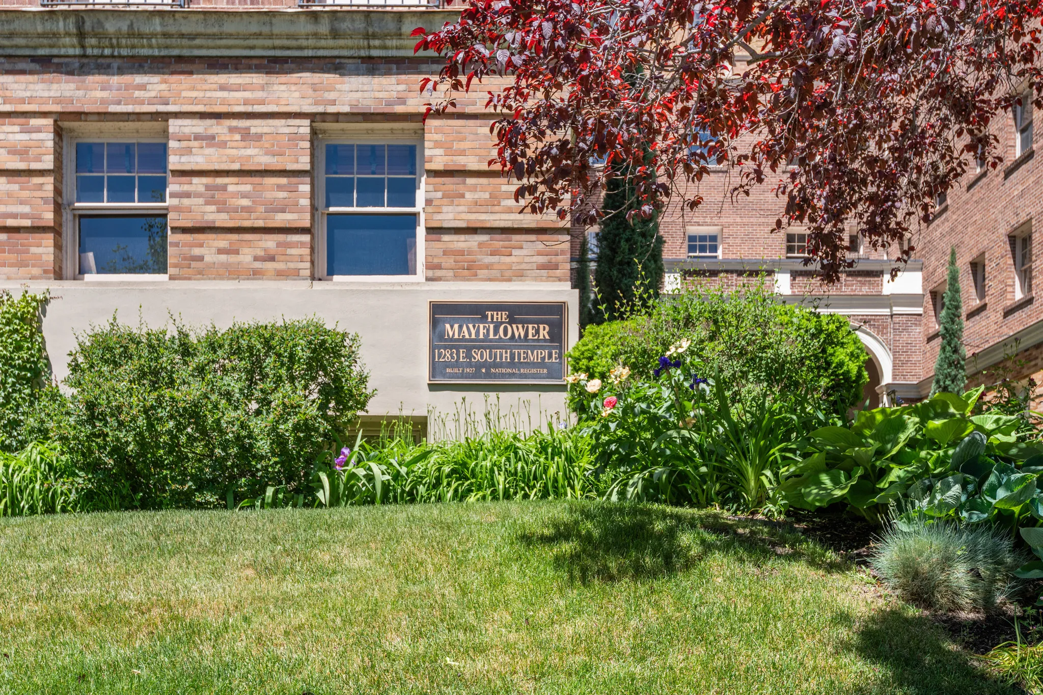 Brick exterior featuring multiple windows, a prominent building sign, and mature landscaping