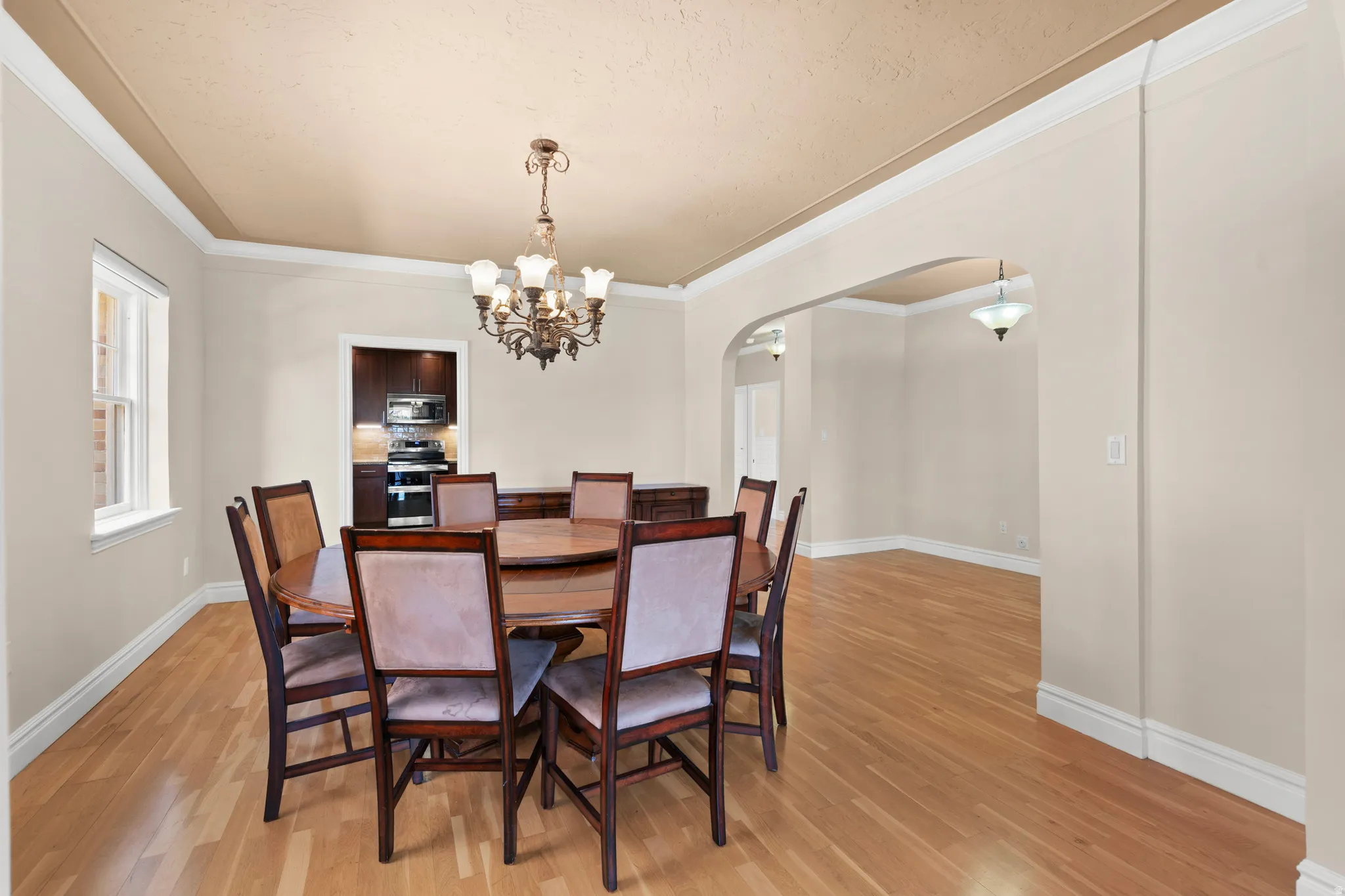 Dining area featuring wood-finish flooring, a traditional chandelier, arched doorways, crown molding, and a window with white trim