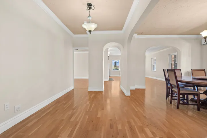 Wood-finish flooring throughout, featuring decorative ceiling fixtures, crown molding, and arched doorways