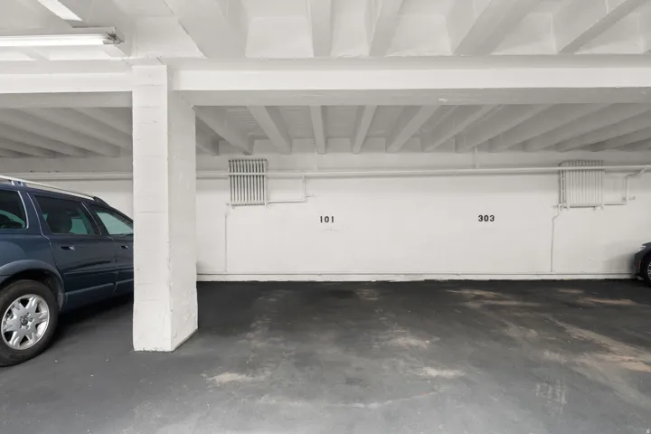Covered parking area featuring concrete flooring, white painted walls, and overhead lighting fixtures