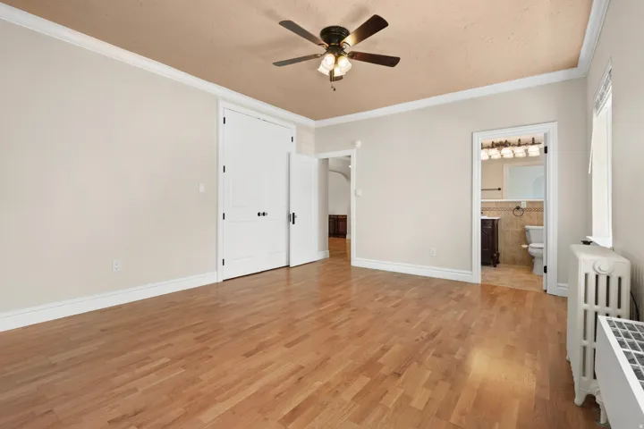 Spacious Master bedroom with wood-finish flooring, crown molding, and a ceiling fan with integrated lighting