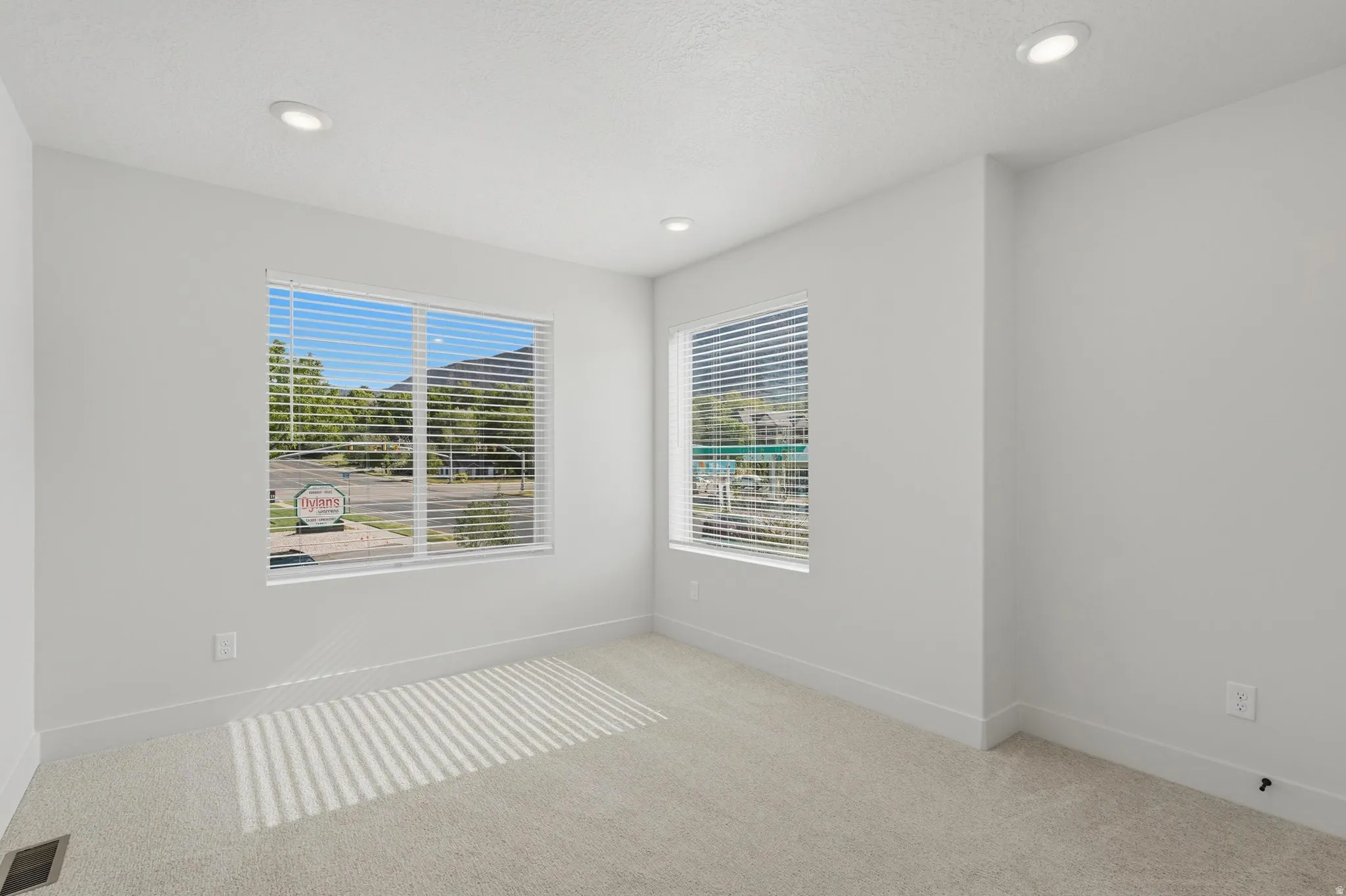 Spacious room featuring neutral carpeting, recessed lighting, white walls, and two large windows with blinds