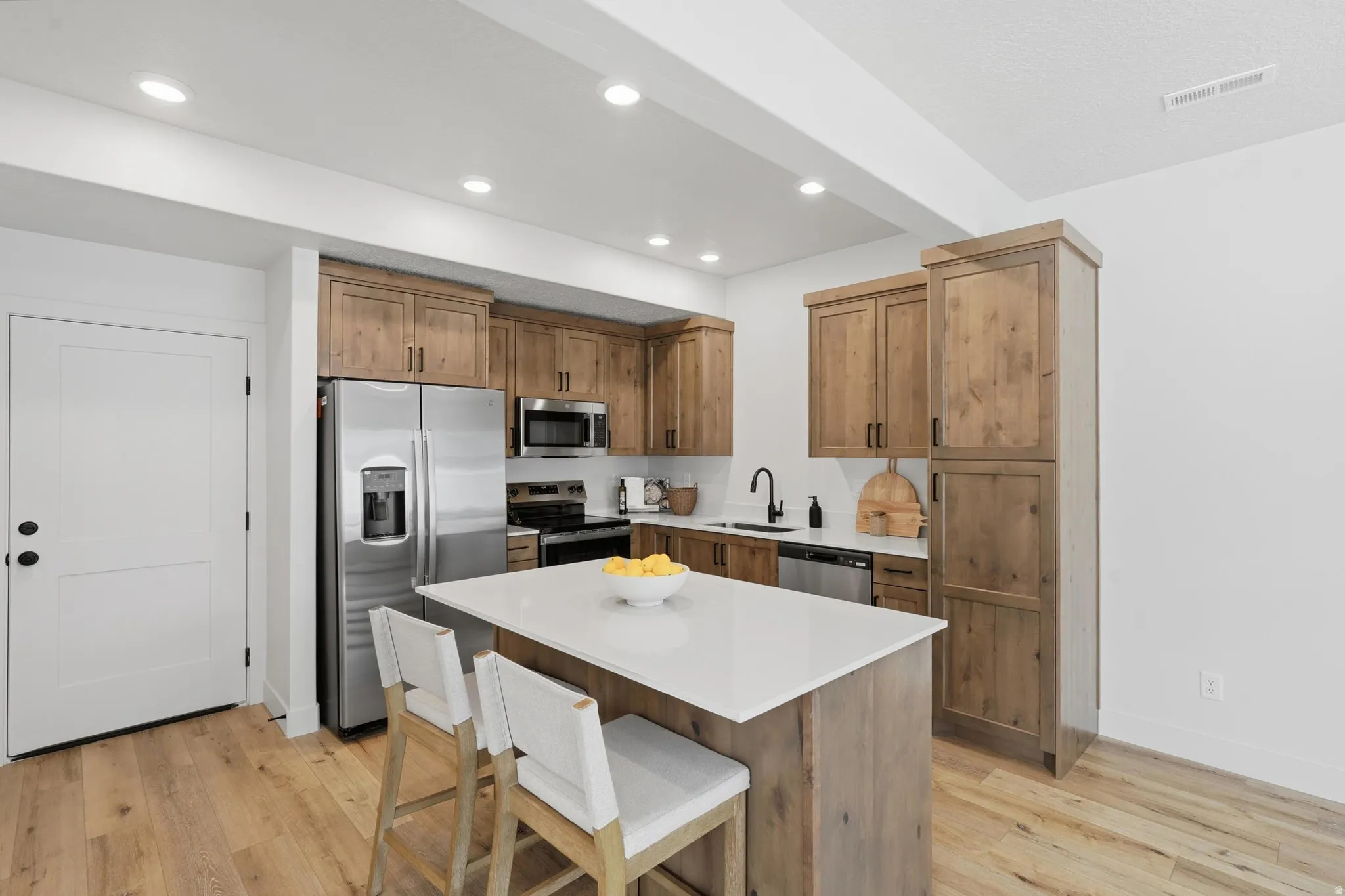 Contemporary kitchen featuring light wood-finish cabinetry and flooring, a white island countertop, stainless steel appliances, and recessed lighting