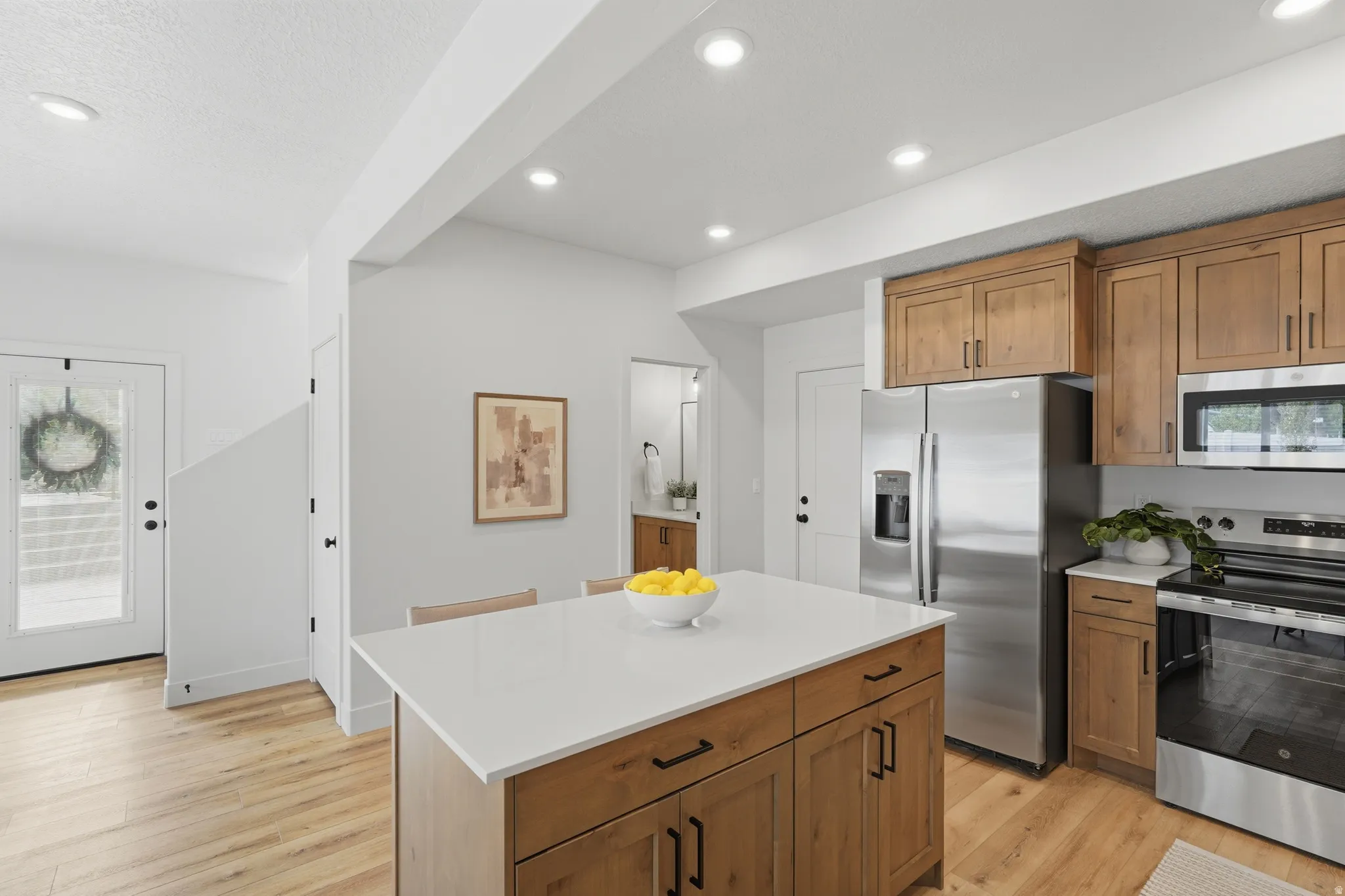 Open-concept kitchen featuring a central island with a white countertop, wood-finish cabinetry, stainless steel appliances, and recessed lighting