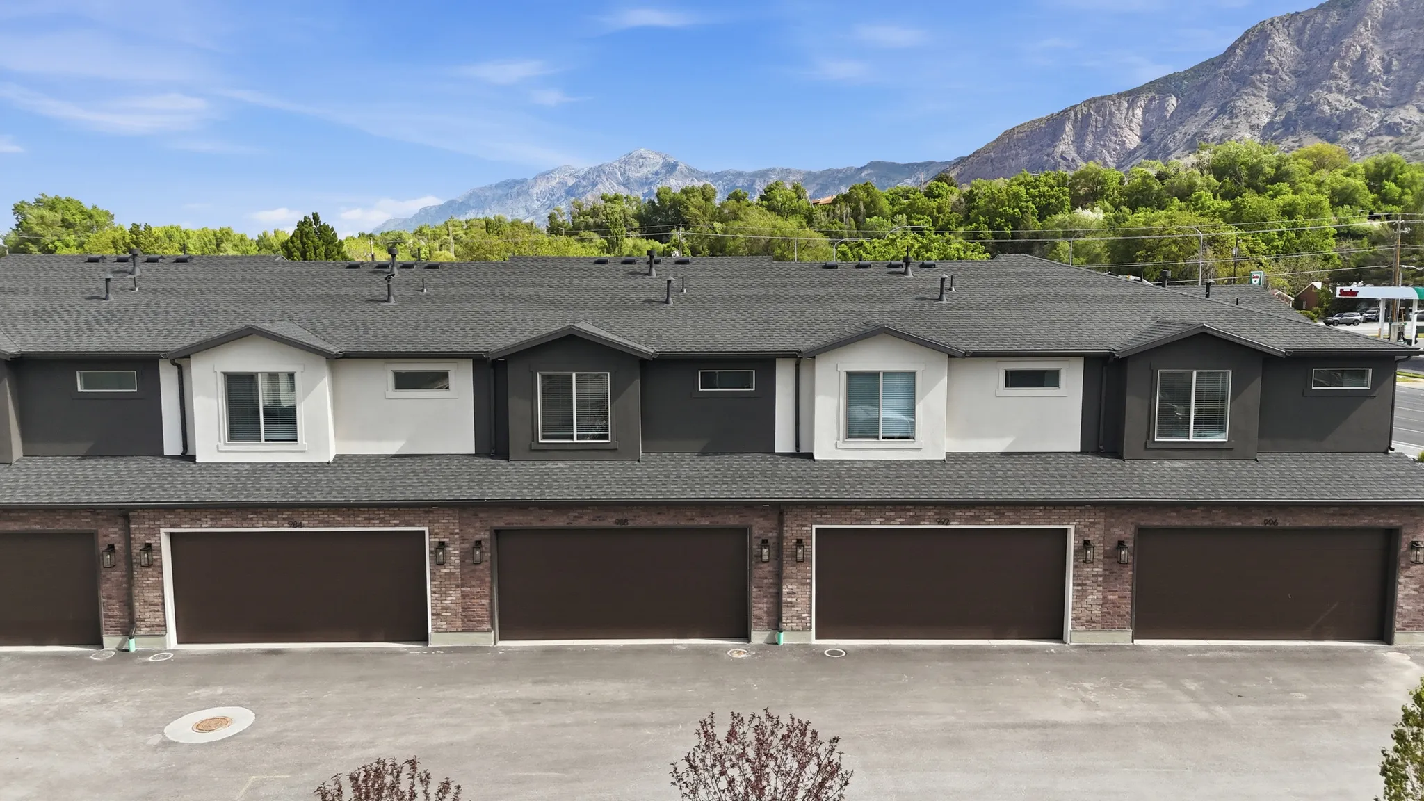 Contemporary townhome exterior featuring a dark gray shingle roof, mixed material facade with brick and stucco, and individual brown garage doors