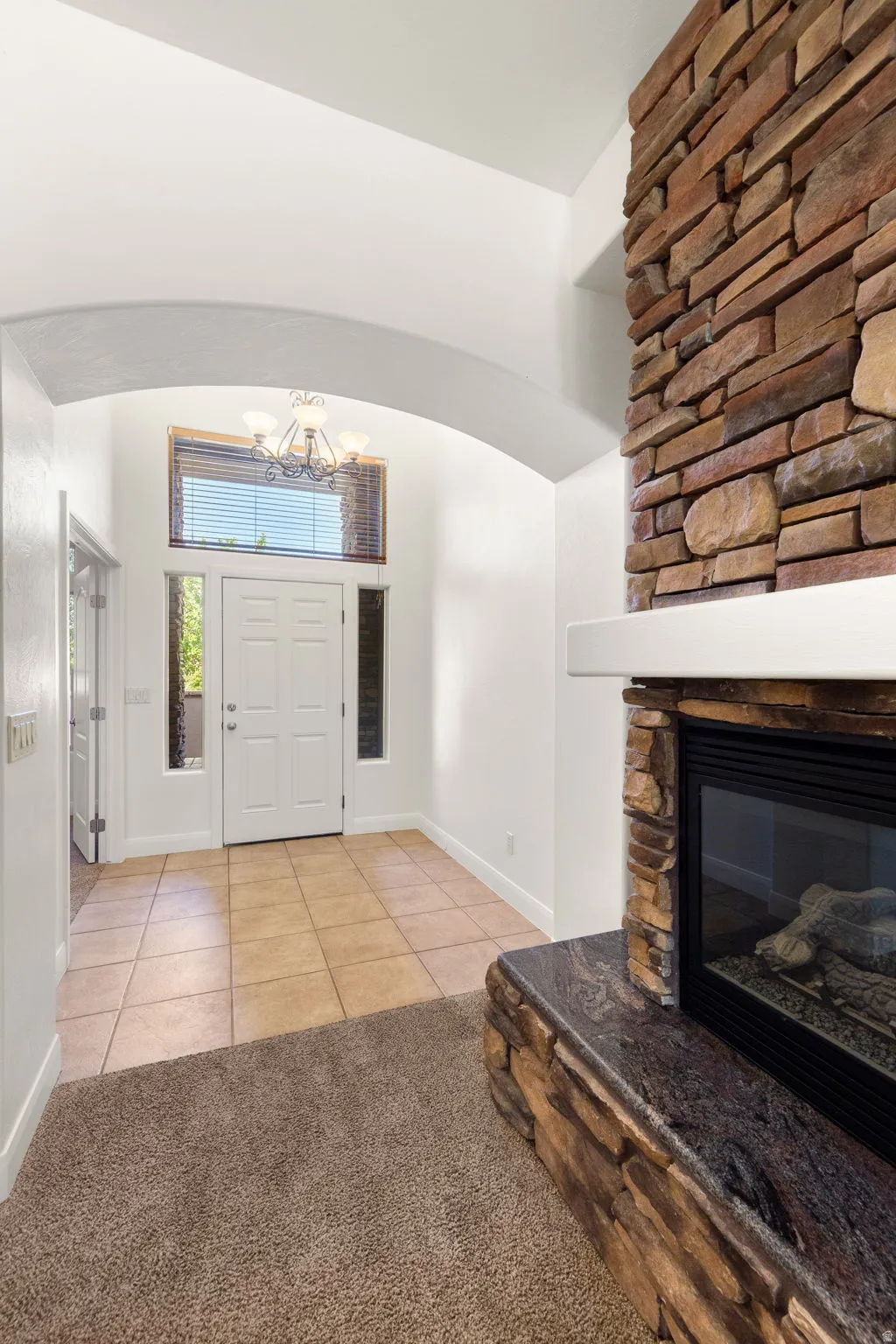 Foyer featuring a stone-clad fireplace with a dark stone hearth, a tiled entry floor, and an arched doorway