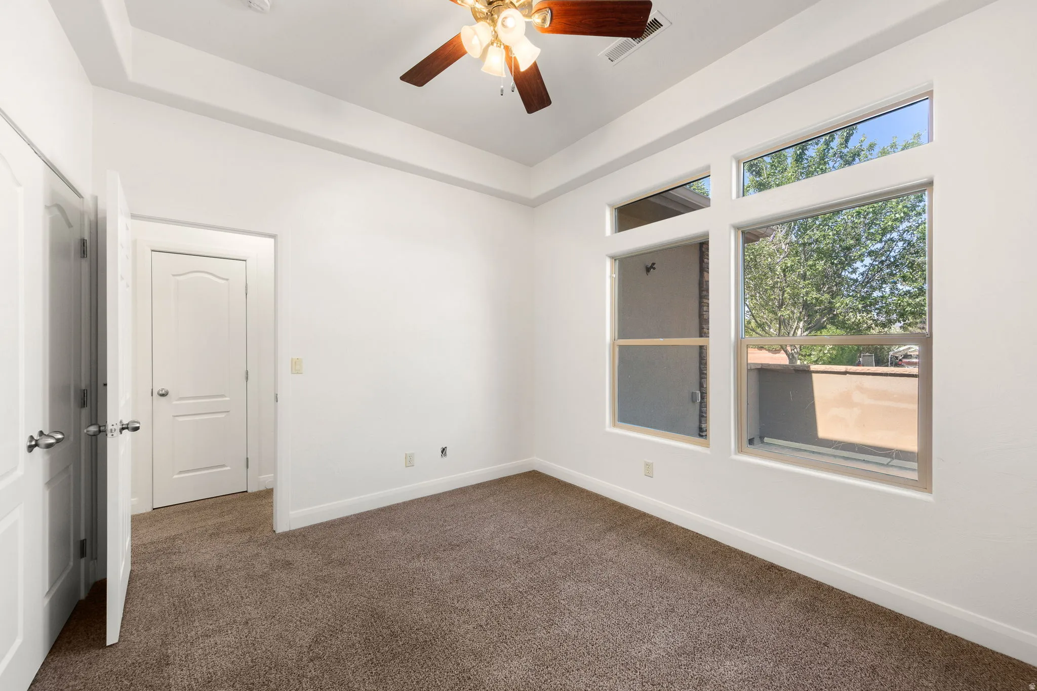Bedroom featuring a ceiling fan with light fixture, tray ceiling, and multiple windows