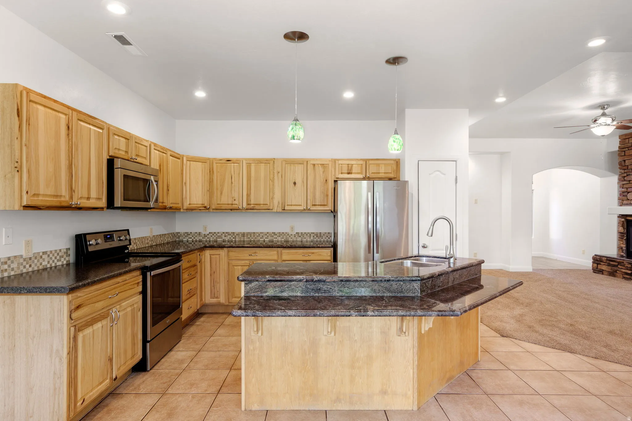 Open-concept kitchen featuring wood cabinetry, stainless steel appliances, and a central island with a built-in sink and extended countertop