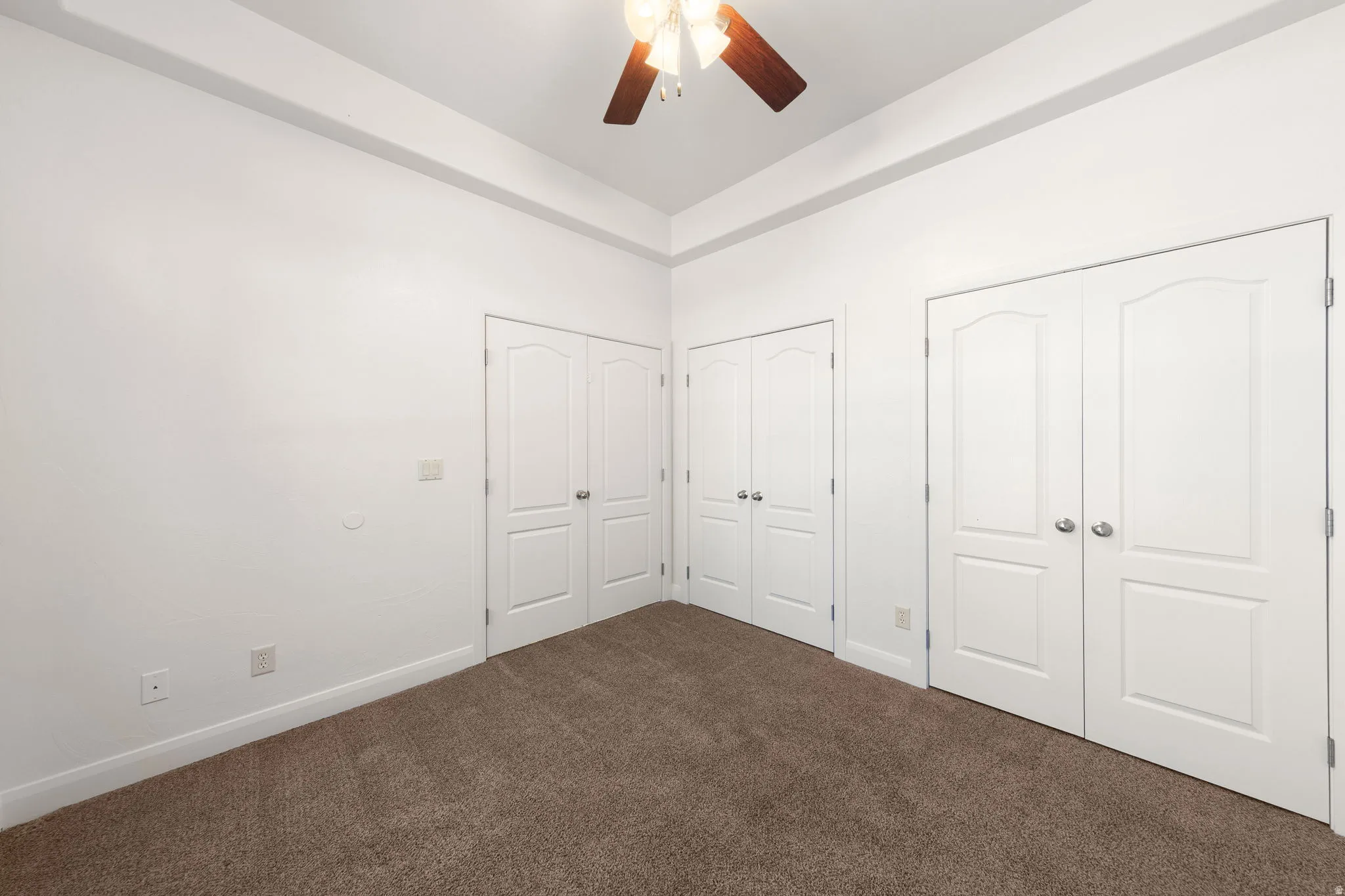 Spacious room featuring multiple white paneled closet doors, warm brown carpeting, and a ceiling fan with integrated lighting