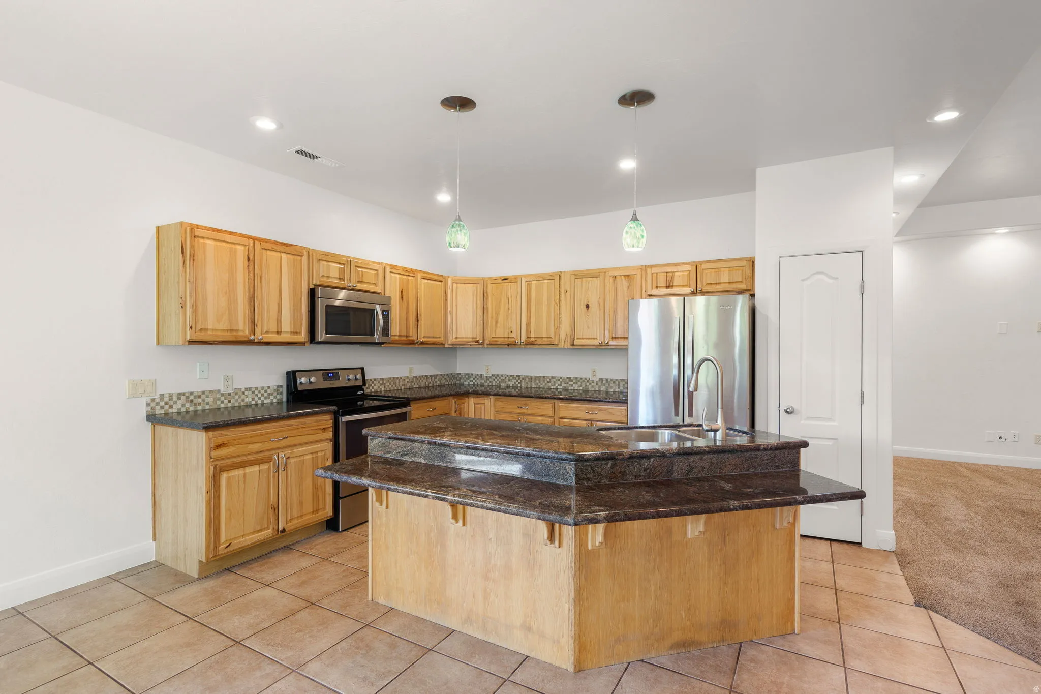 Spacious kitchen featuring natural wood cabinetry, granite countertops, stainless steel appliances, and a central island with integrated sink