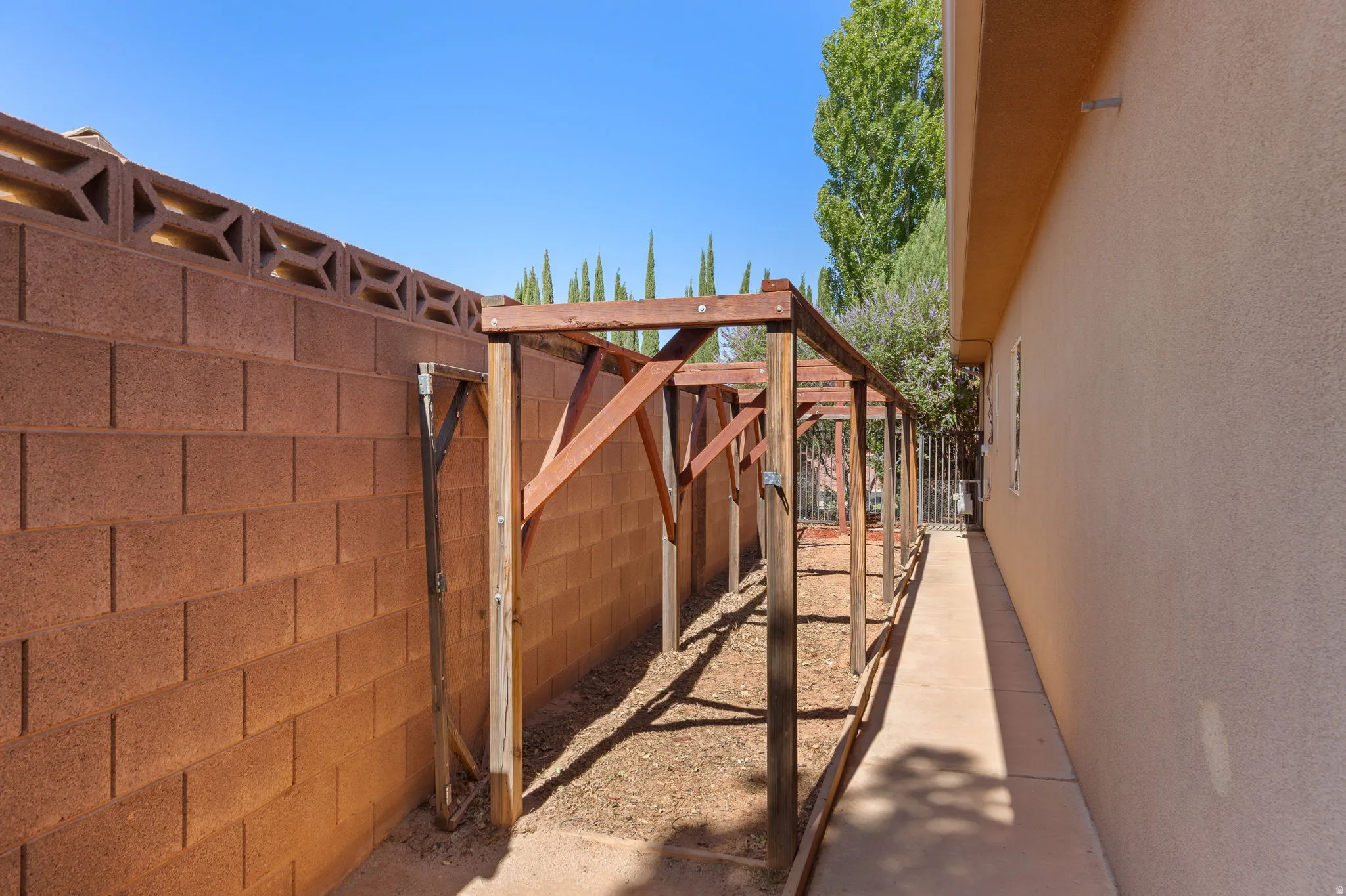 Side yard featuring a wood arbor structure, stucco exterior wall, concrete walkway, and block wall with decorative top elements