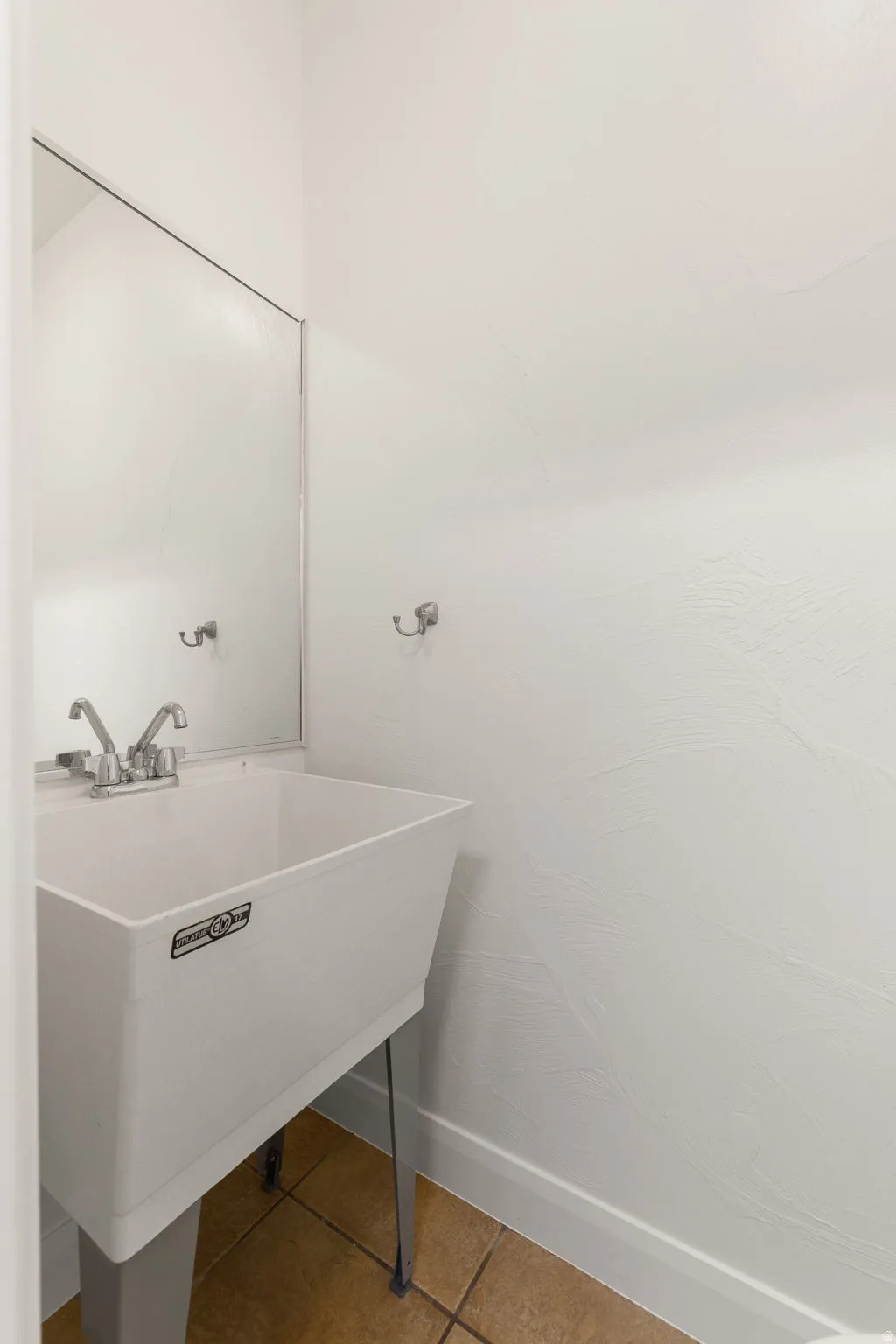 Utility sink with chrome faucet hardware, white walls, and light-toned tile flooring