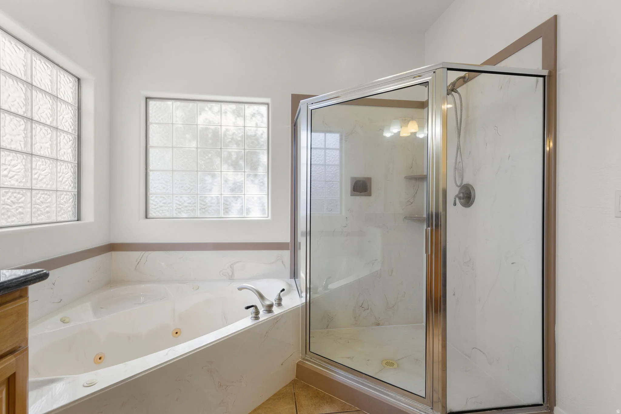 Corner jetted tub with tiled surround, glass block windows, and a separate glass-enclosed shower