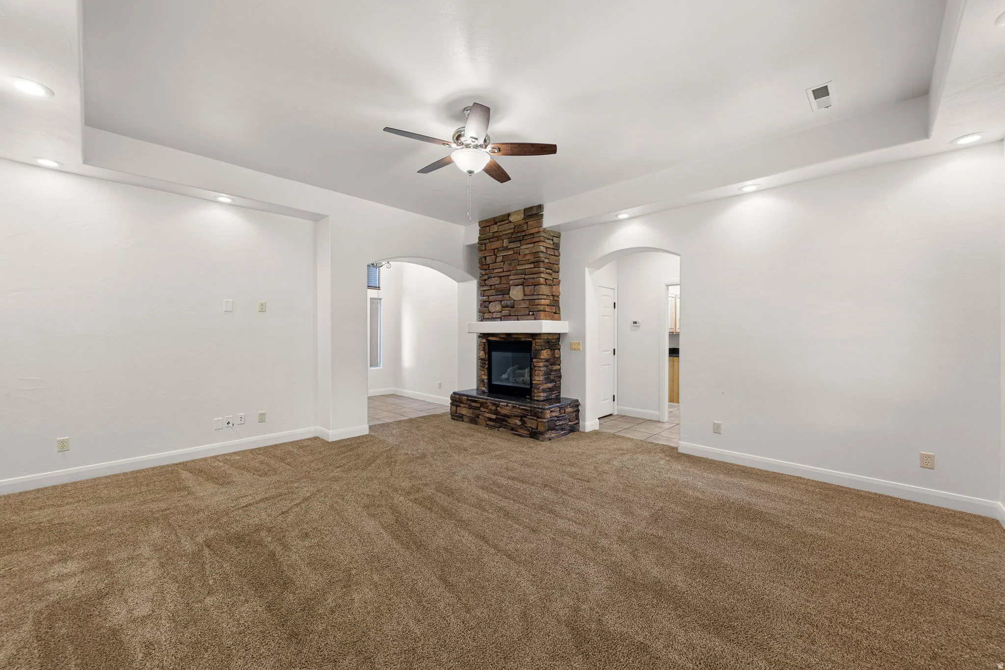 Living area featuring a stone-clad fireplace with a white mantel, arched doorways, a ceiling fan, and recessed lighting