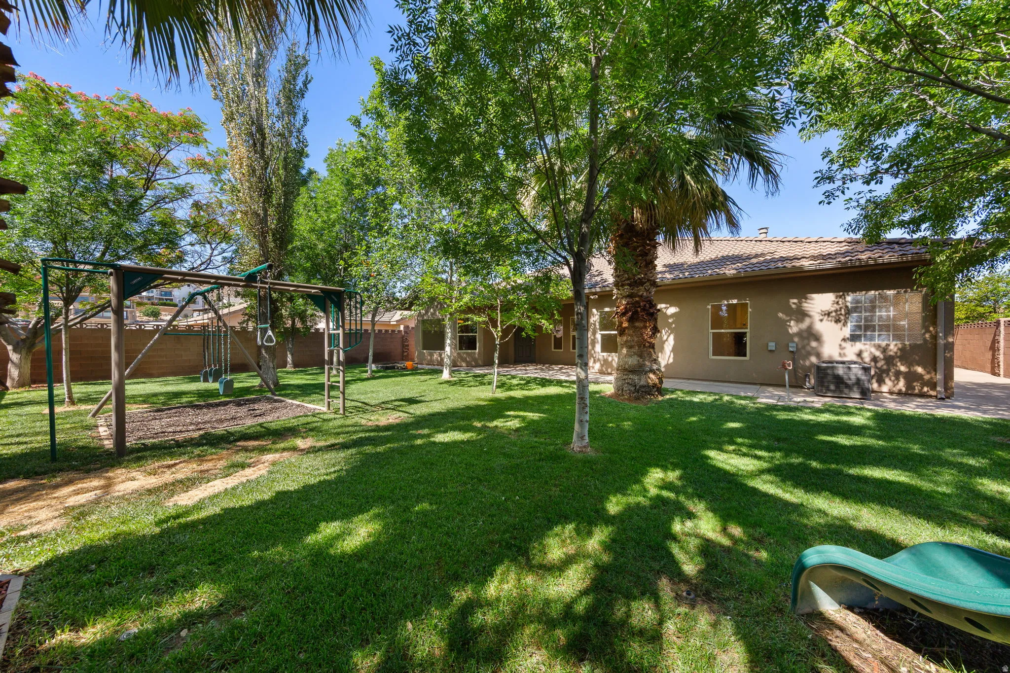 Expansive backyard featuring a large lawn, mature trees, wood privacy fencing, and a stucco exterior with multiple windows