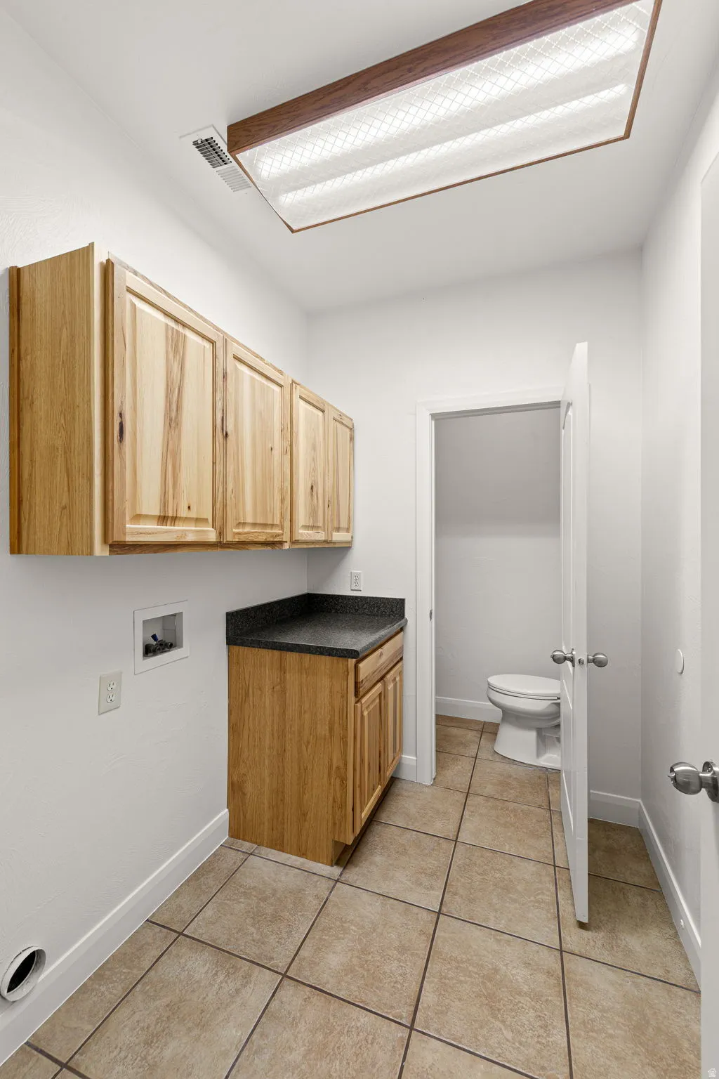 Functional utility room featuring wood-finish cabinetry, a dark countertop, and tile flooring